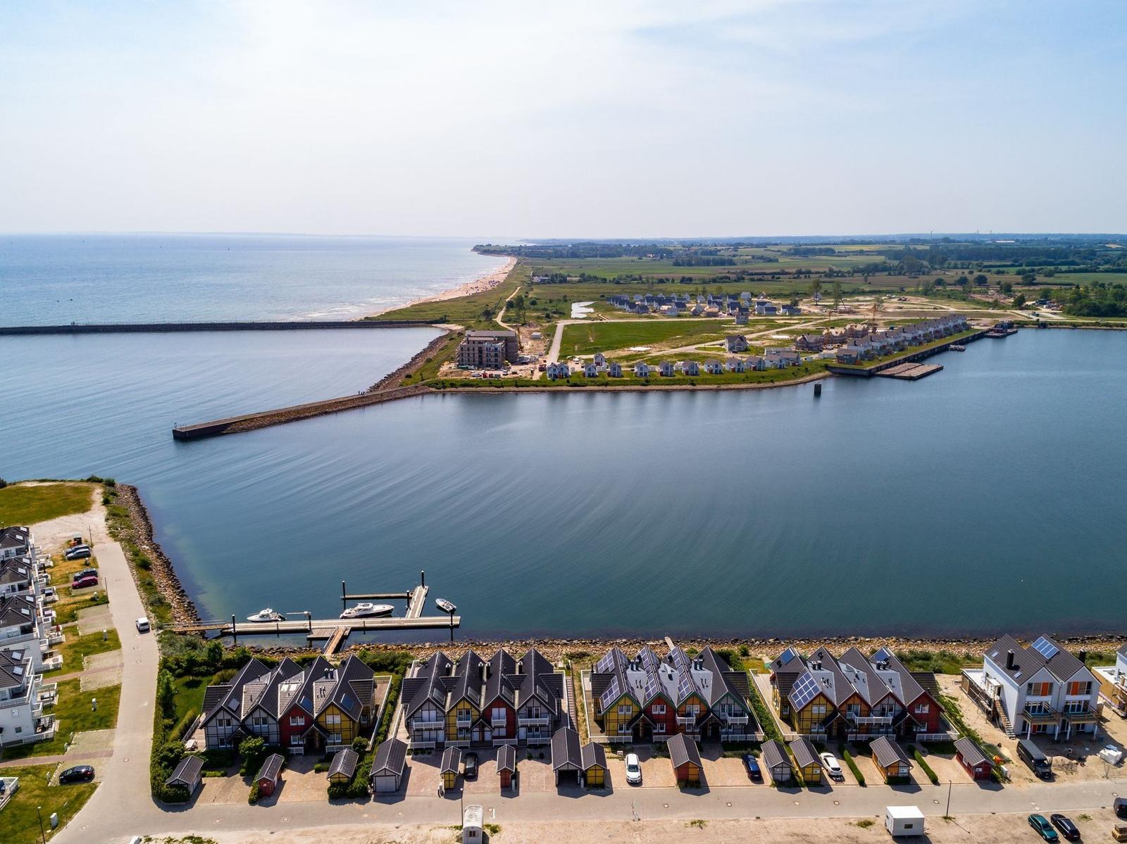 Aerial view of coastal homes near beach and harbor with boats and clear blue water.