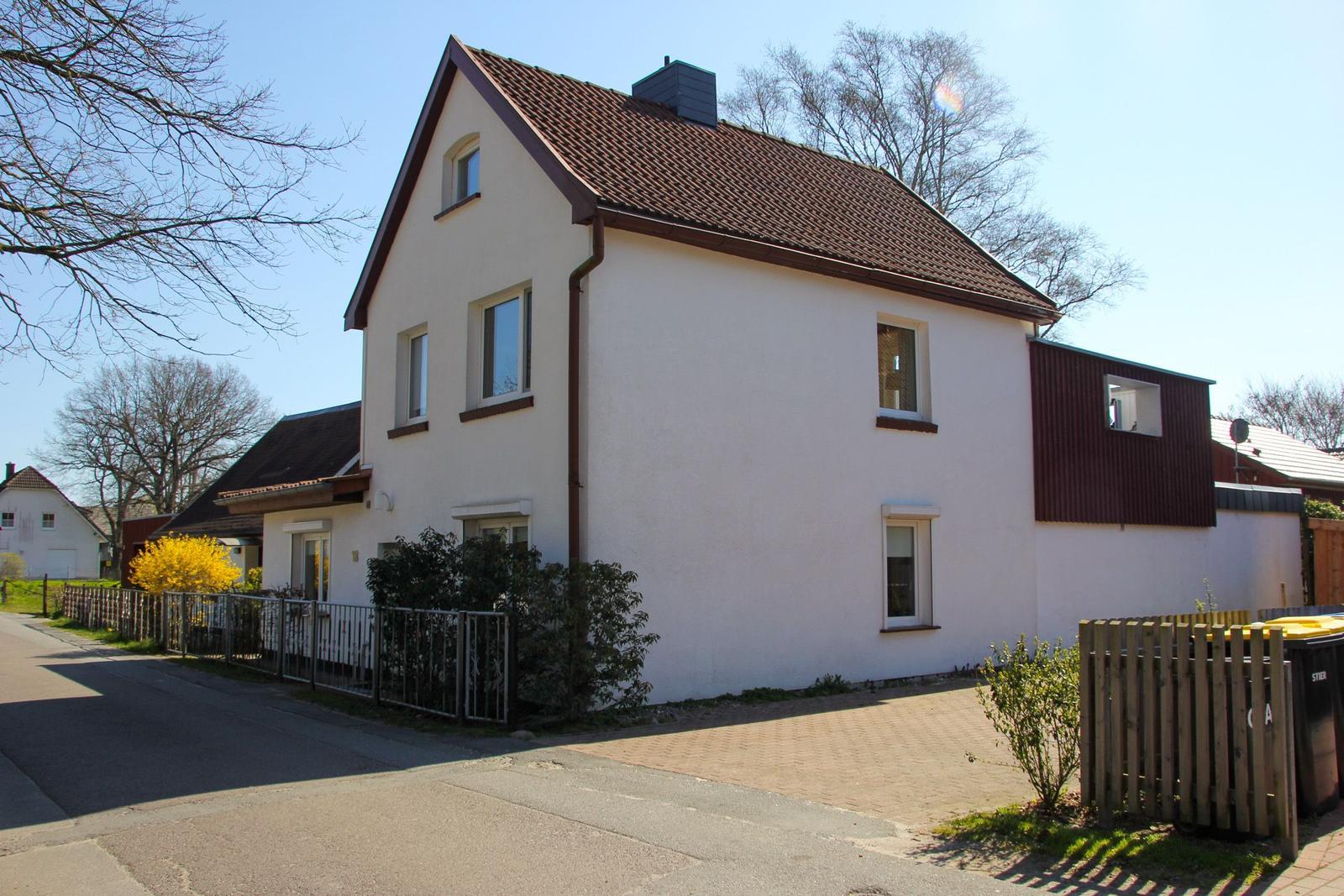 House with white facade and red roof, surrounded by greenery and trees.