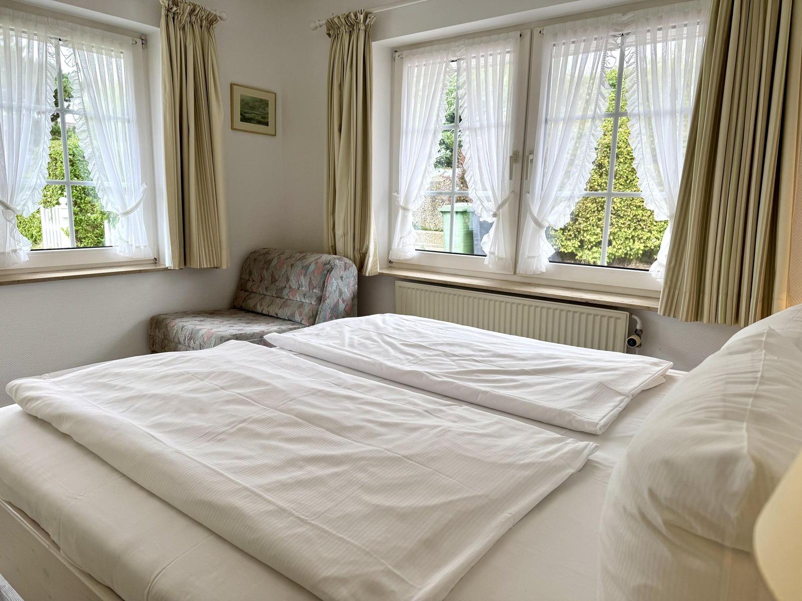 Bedroom with double bed, two lattice windows and a patterned armchair.
