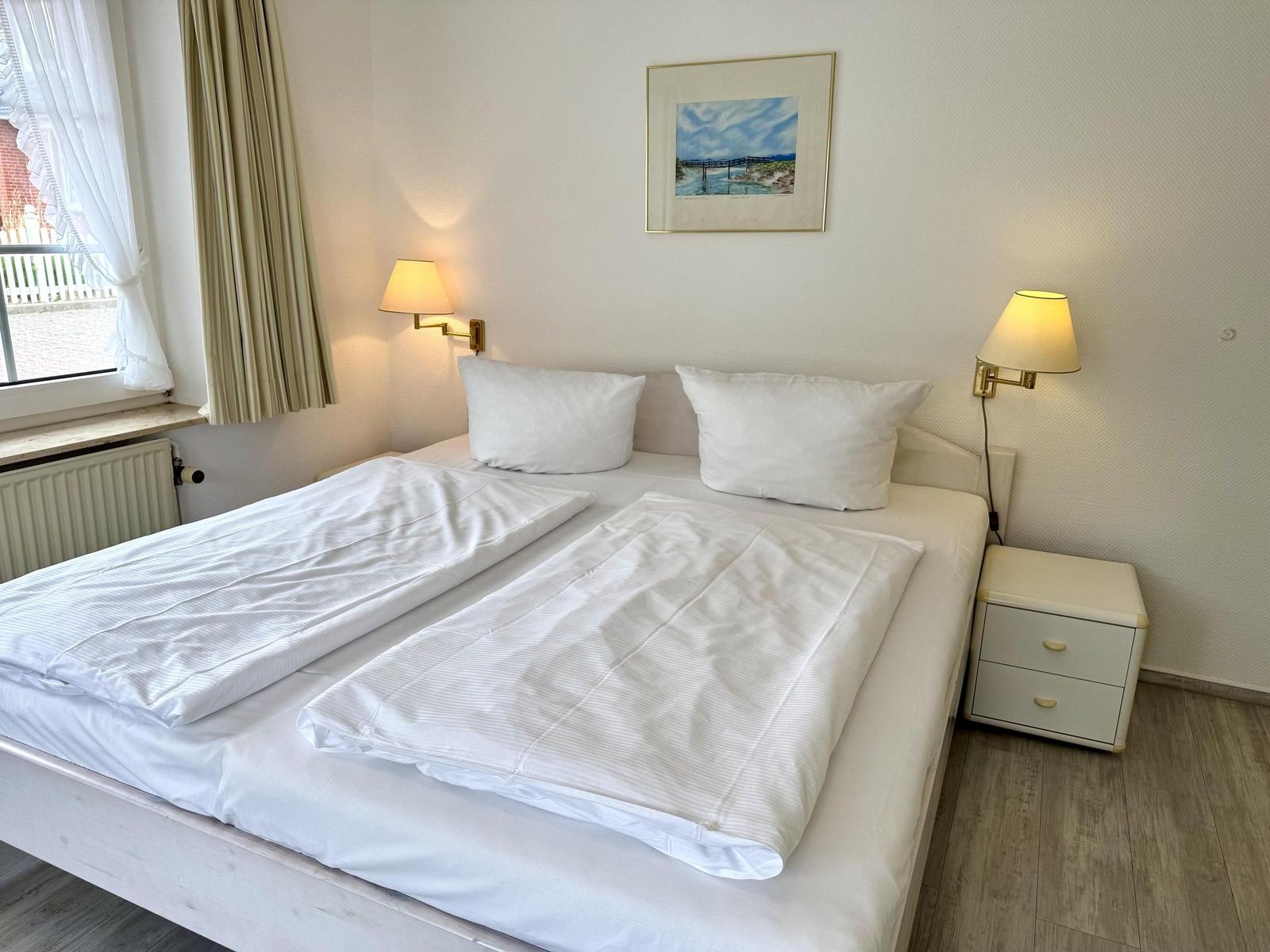 Double bed with two wall lamps, nightstand and window with curtain.