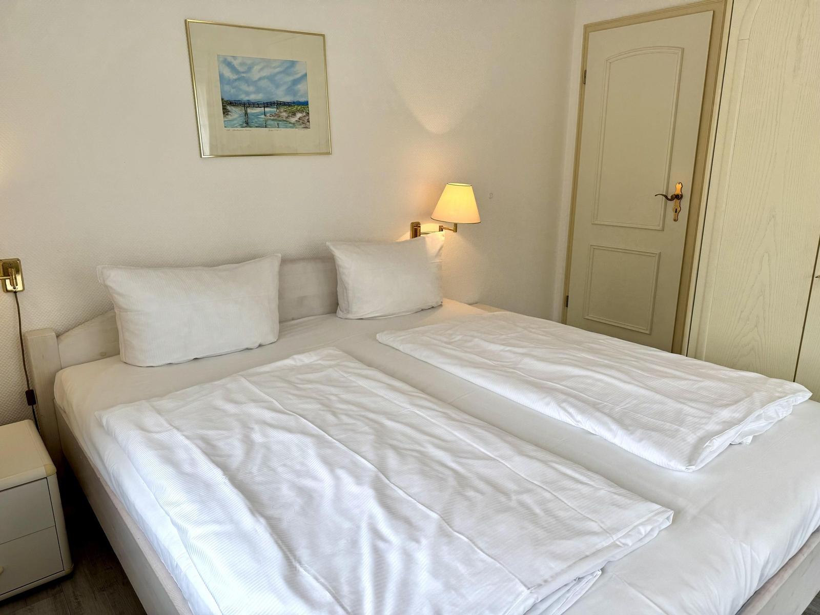 Double bed with white bedding, wall lamp and framed coastal picture.
