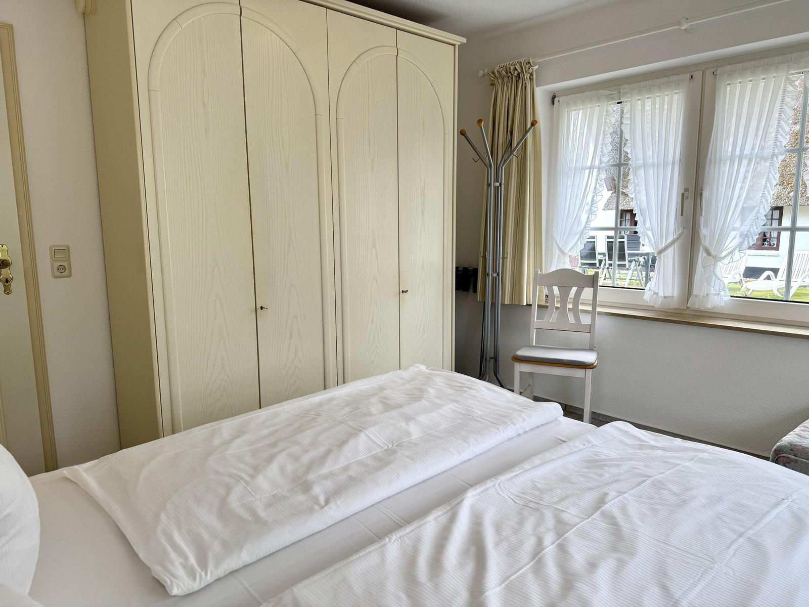 Bedroom with white bed, large wardrobe, chair and window.
