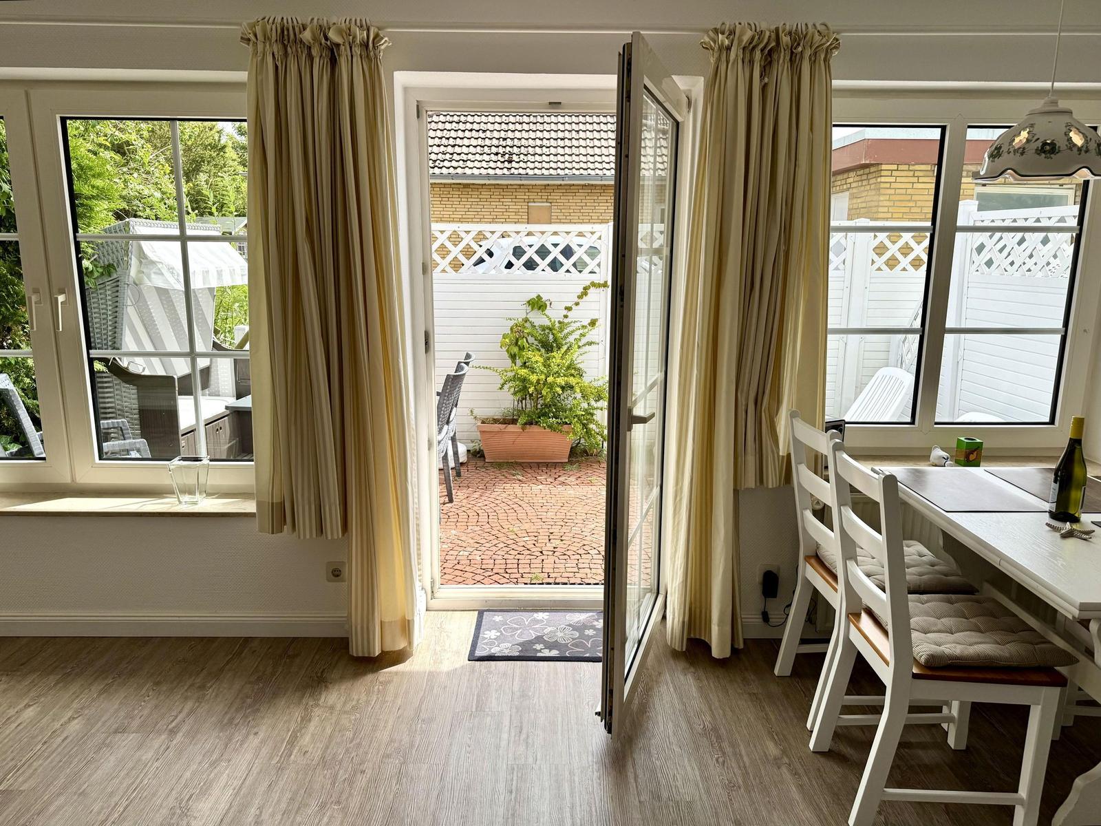 Dining area with white table, open door and beach chair on the terrace.