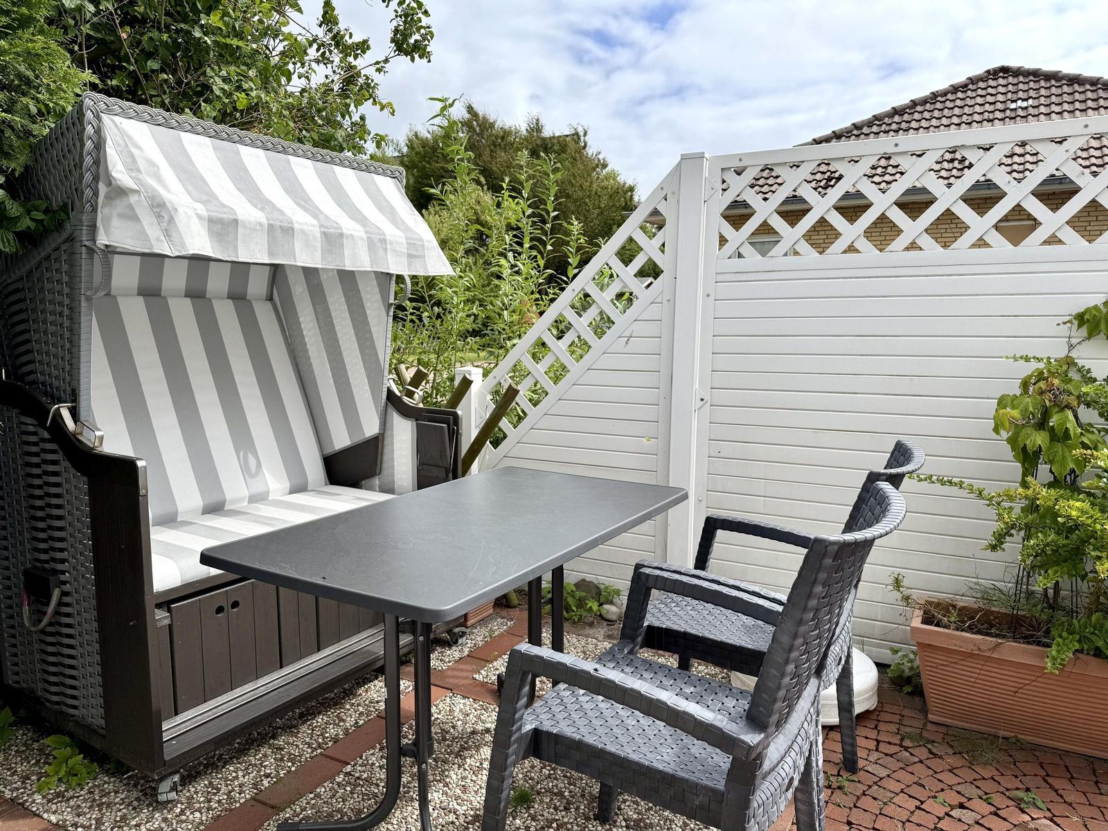 Terrace with beach chair, table, rattan armchairs and white fence.