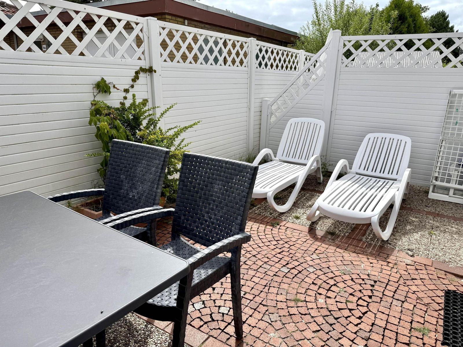 Terrace with paving, dark chairs, white loungers and slatted fence.