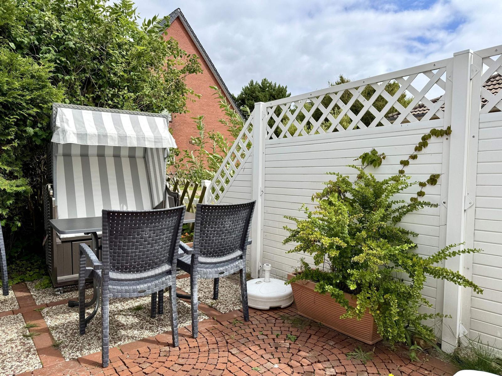Terrace with hooded beach chair, grey wicker chairs and white fence.