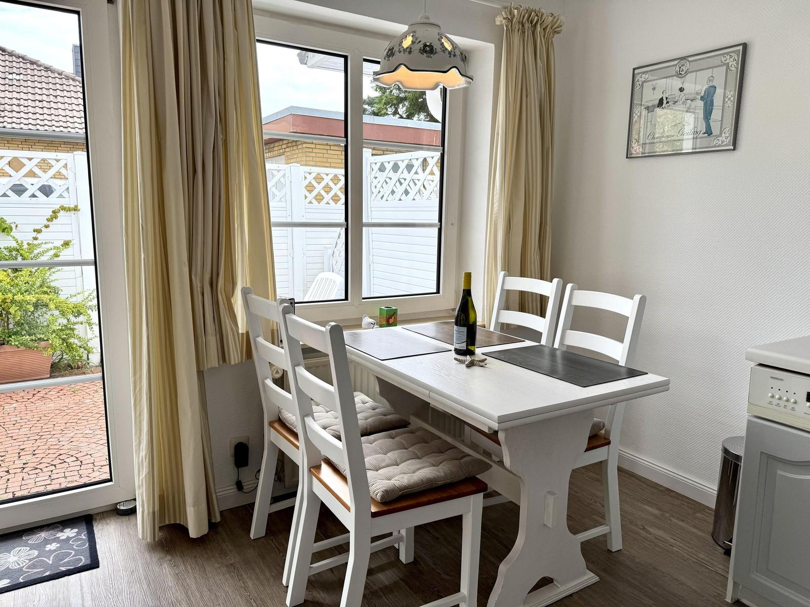 Dining area with white wooden table, four chairs and terrace door.