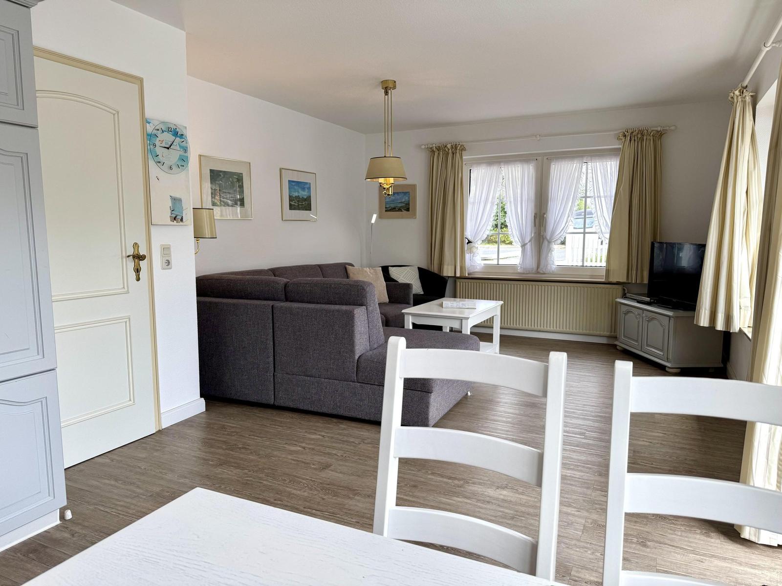 Living area with grey corner sofa, coffee table, TV and dining chairs.