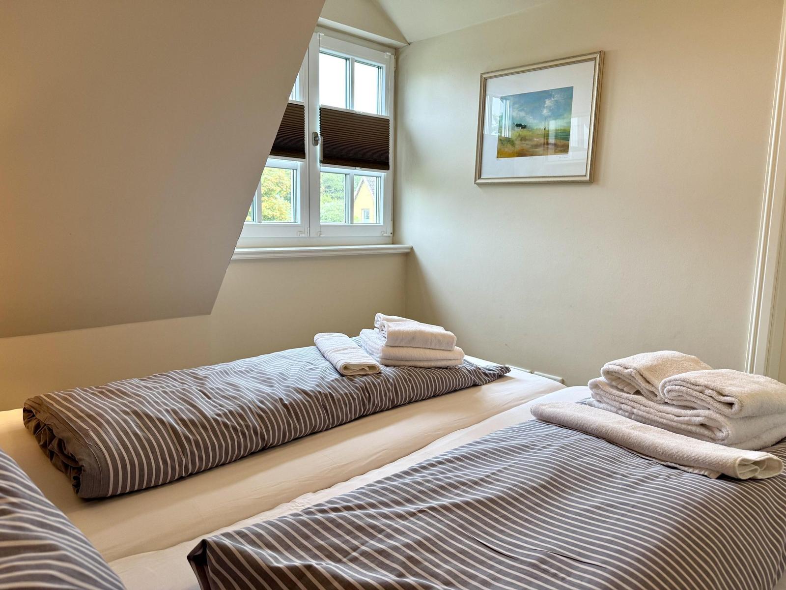Schlafzimmer mit zwei Betten, gestreifter Bettwäsche, Handtüchern und Fenster.
