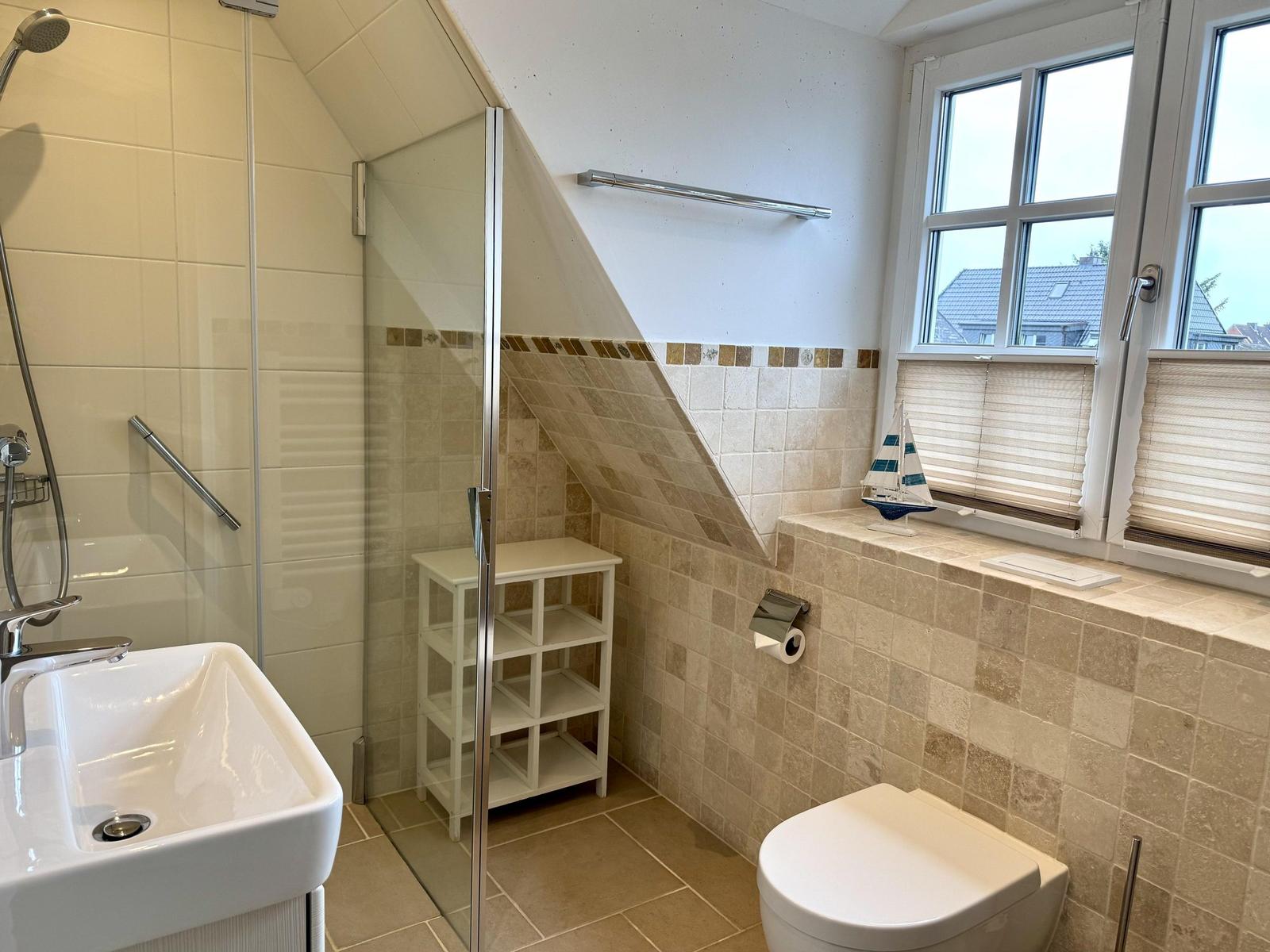 Bad unter Dachschräge mit Dusche, WC, Waschbecken und Fenster mit Plissee.