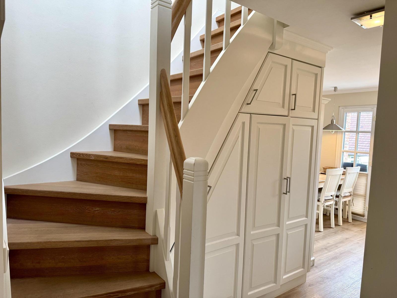Holztreppe mit weißem Geländer und weißen Einbauschränken unter den Stufen.