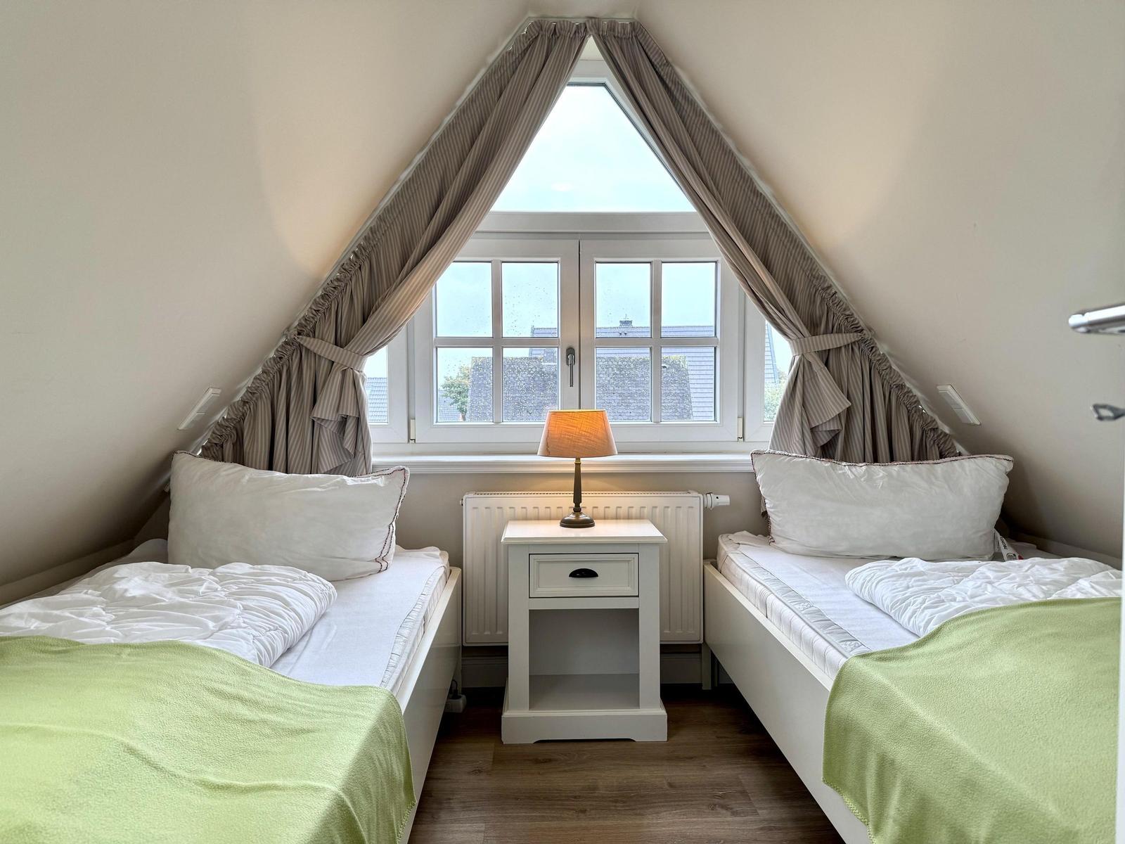 Schlafzimmer mit zwei Einzelbetten, Nachttisch und Fenster unter spitzer Dachschräge.