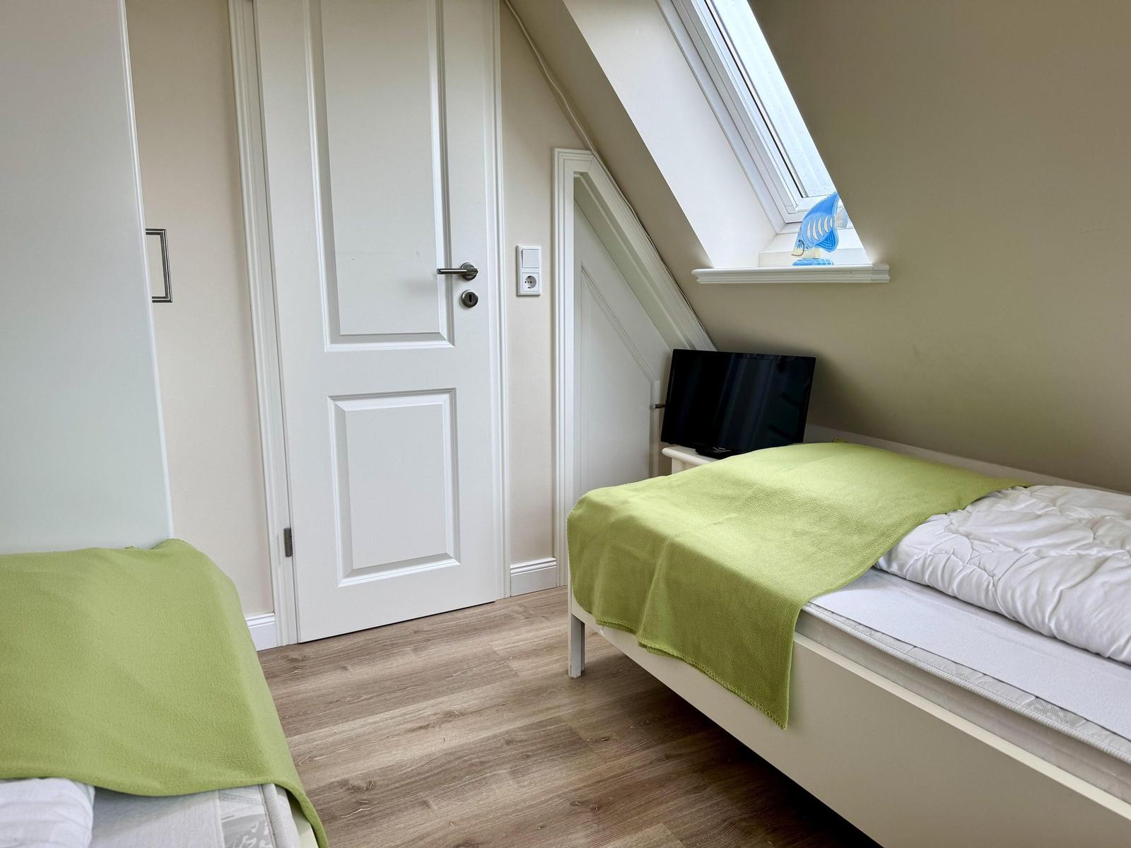 Dachschlafzimmer mit zwei Einzelbetten, hellgrünen Decken, Dachfenster und Fernseher.