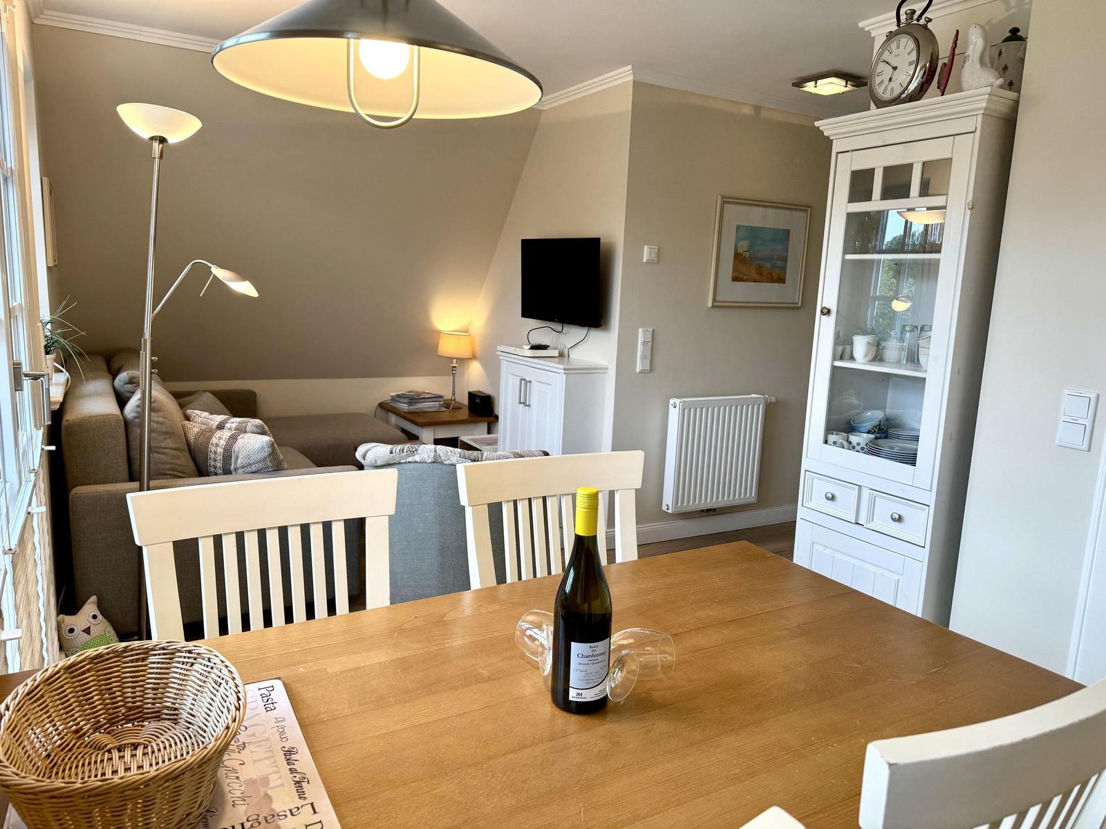 Essbereich mit Holztisch, weißer Vitrine, Ecksofa und Fernseher unter Dachschräge.