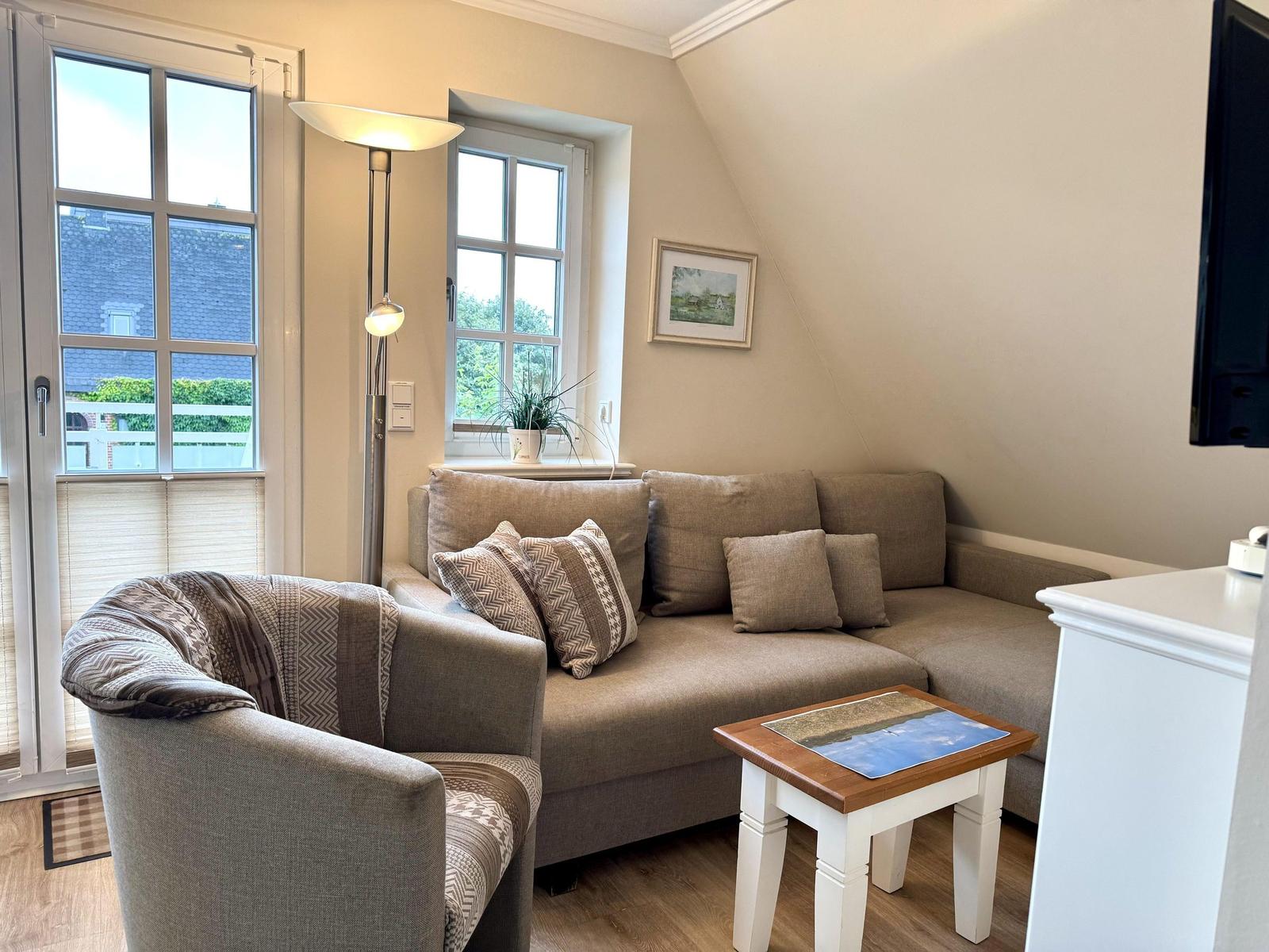 Wohnbereich mit grauem Ecksofa, Sessel, Couchtisch und Stehlampe unter Dachschräge.