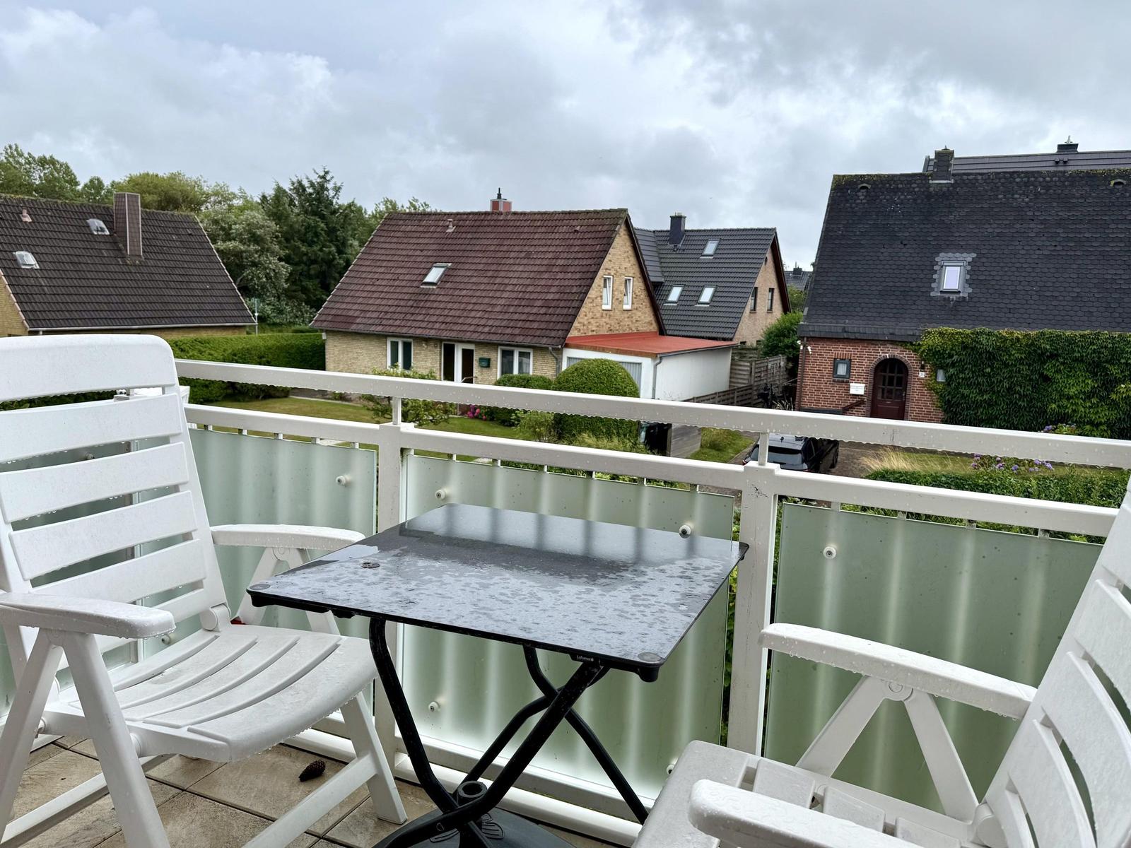 Balkon mit weißen Stühlen, schwarzem Tisch und Blick auf Nachbarhäuser.