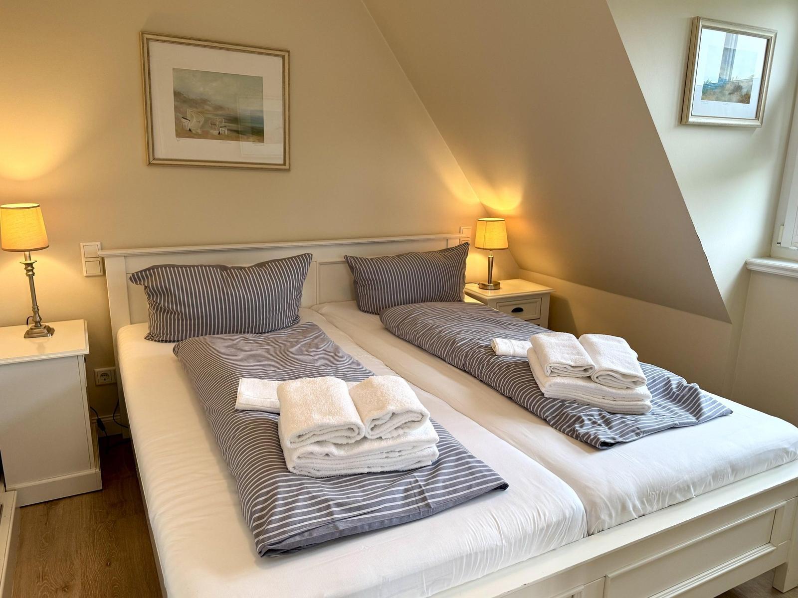 Doppelbett mit gestreifter Bettwäsche, Handtüchern und Nachttischlampen unter Dachschräge.