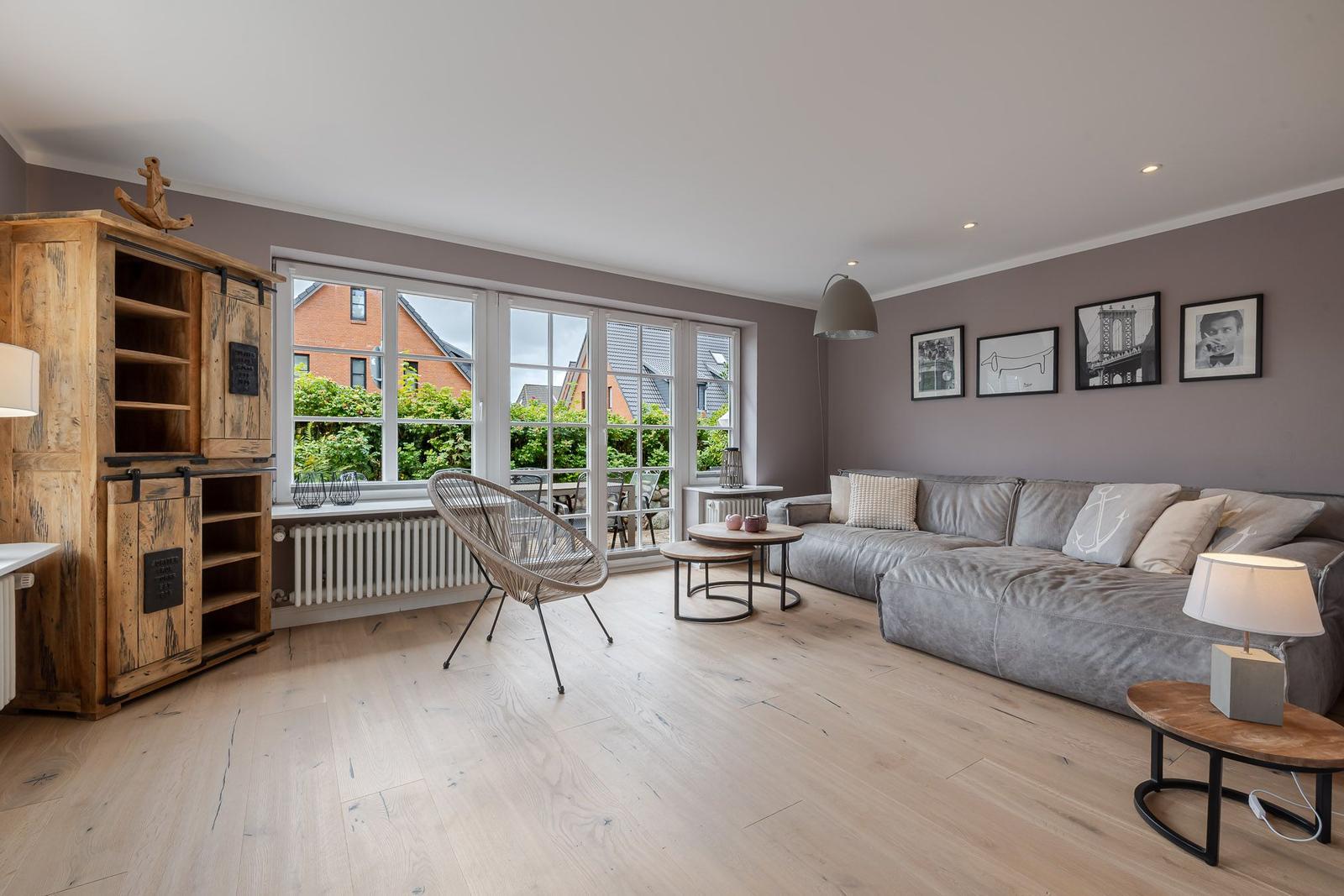 Wohnzimmer mit grauem Sofa, rustikalem Holzschrank und großer Fensterfront.