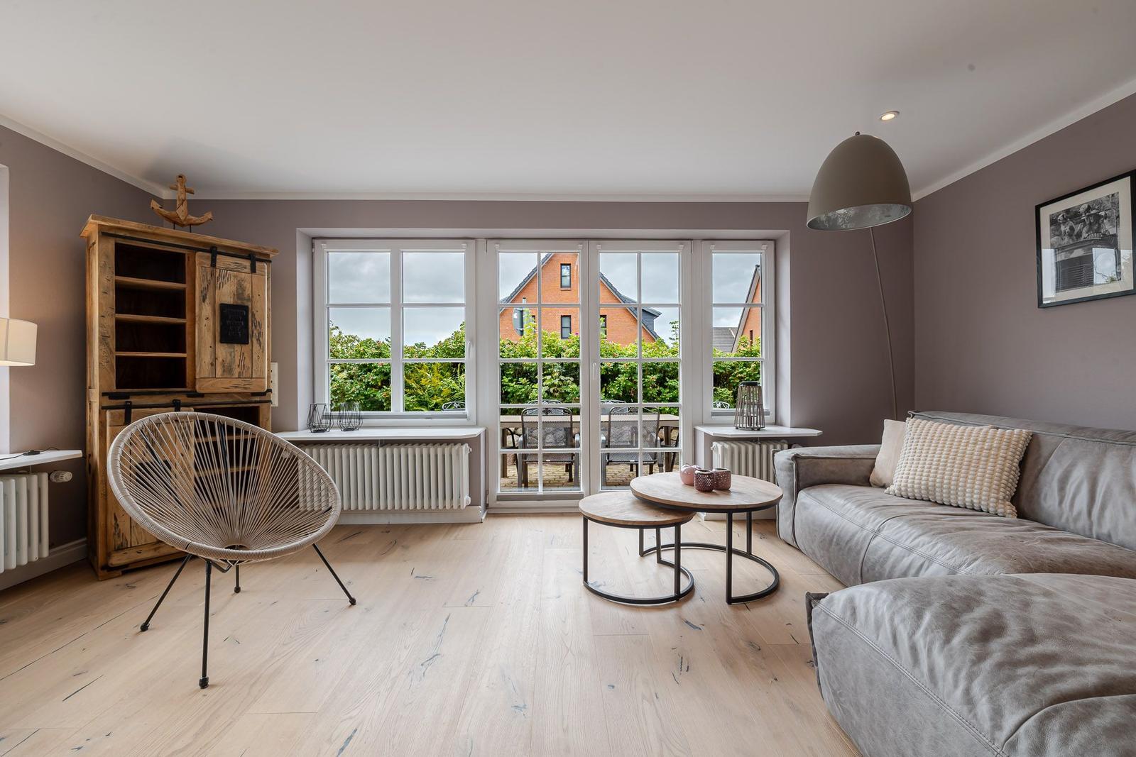 Wohnzimmer mit grauem Sofa, runden Holztischen, Rundsessel und Holzschrank.