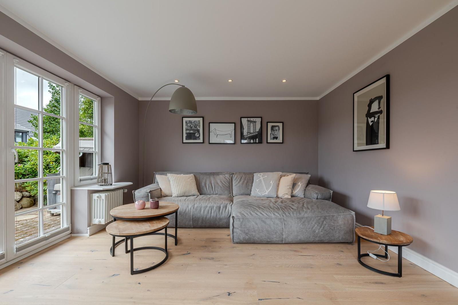 Wohnzimmer mit grauem Ecksofa, runden Holztischen, Stehlampe und Wandbildern.