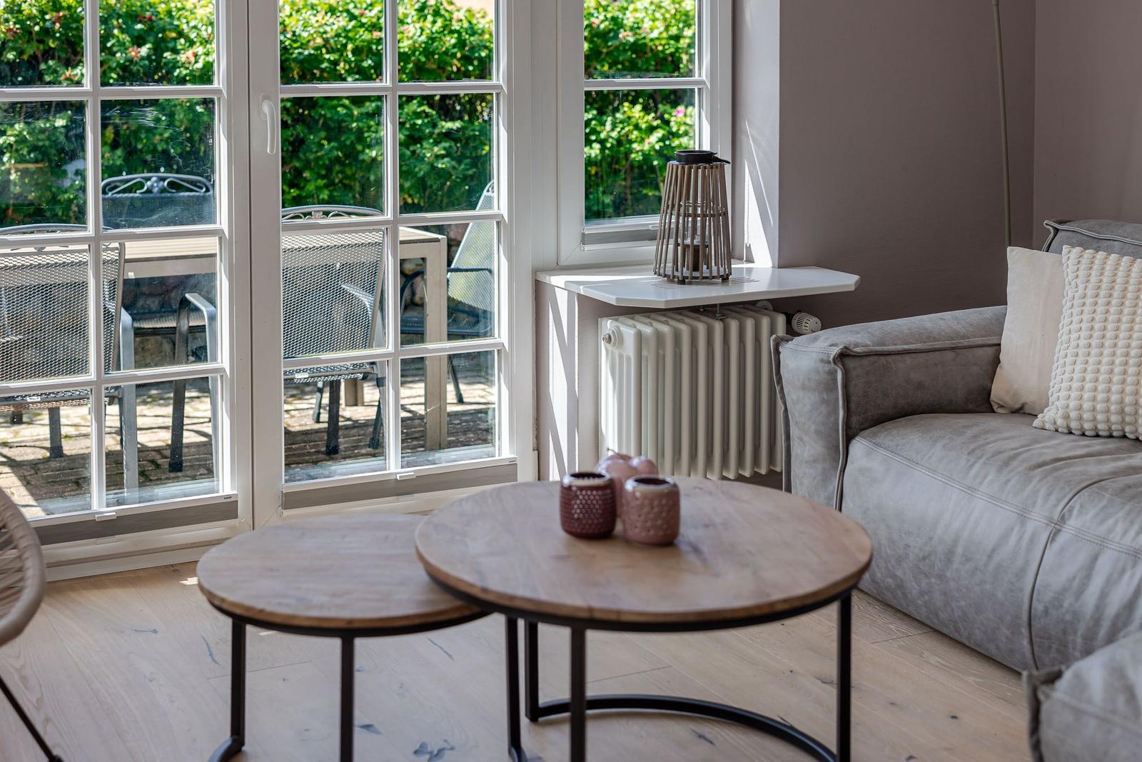 Runde Holztische vor Sofa, Sprossentür zur Terrasse und weißer Heizkörper.