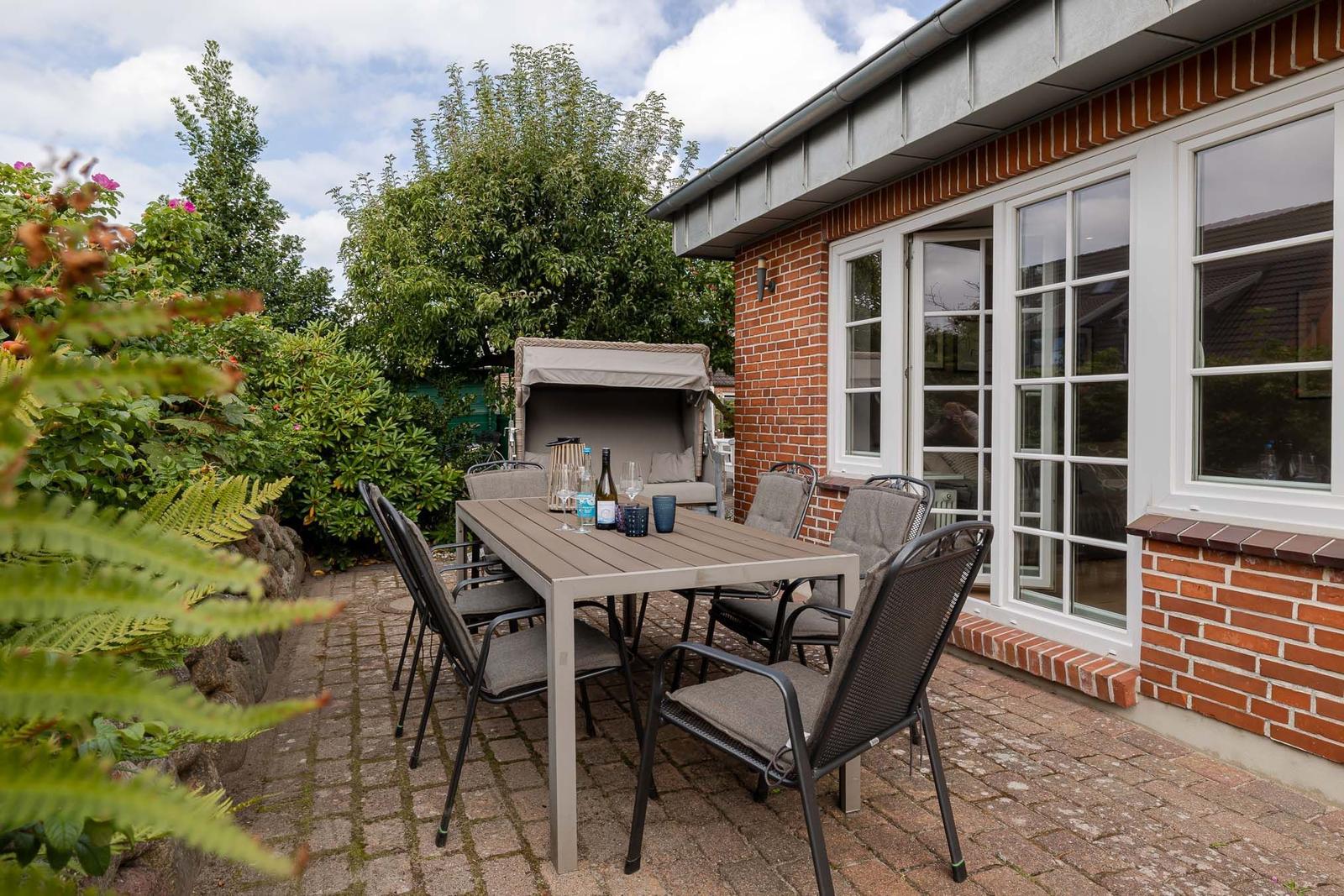 Terrasse am Backsteinhaus mit Esstisch, Stühlen, Strandkorb und Farnen davor.