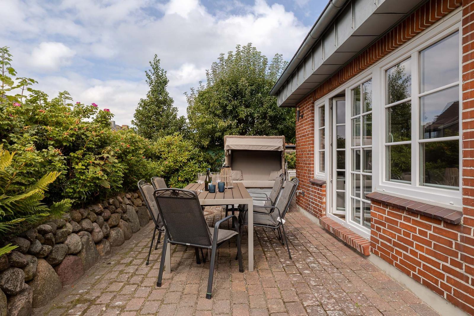 Terrasse mit Holztisch, Stühlen, Strandkorb und Natursteinmauer am Backsteinhaus.