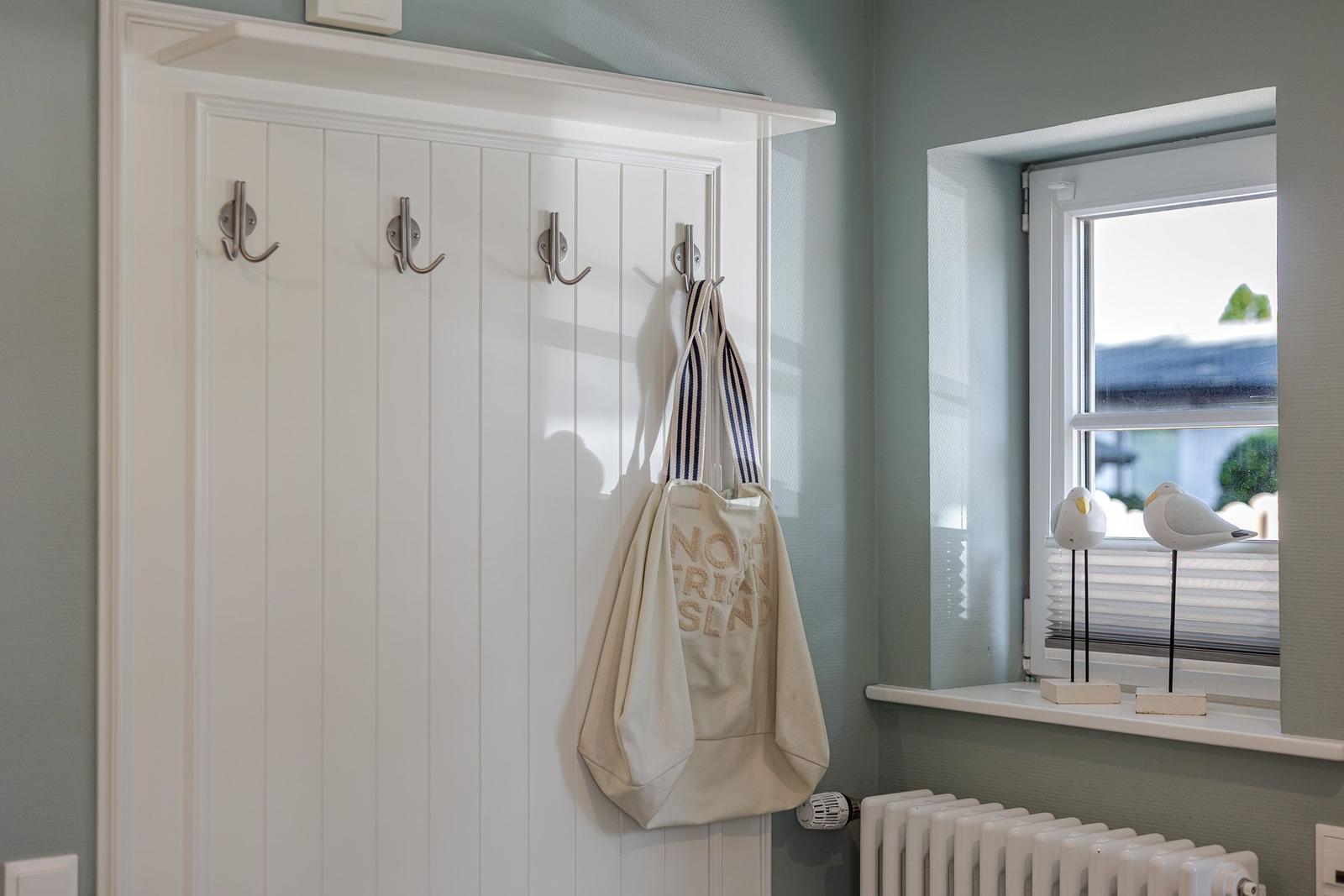 Weiße Garderobe mit Haken und Stofftasche neben Fenster mit Dekovögeln.