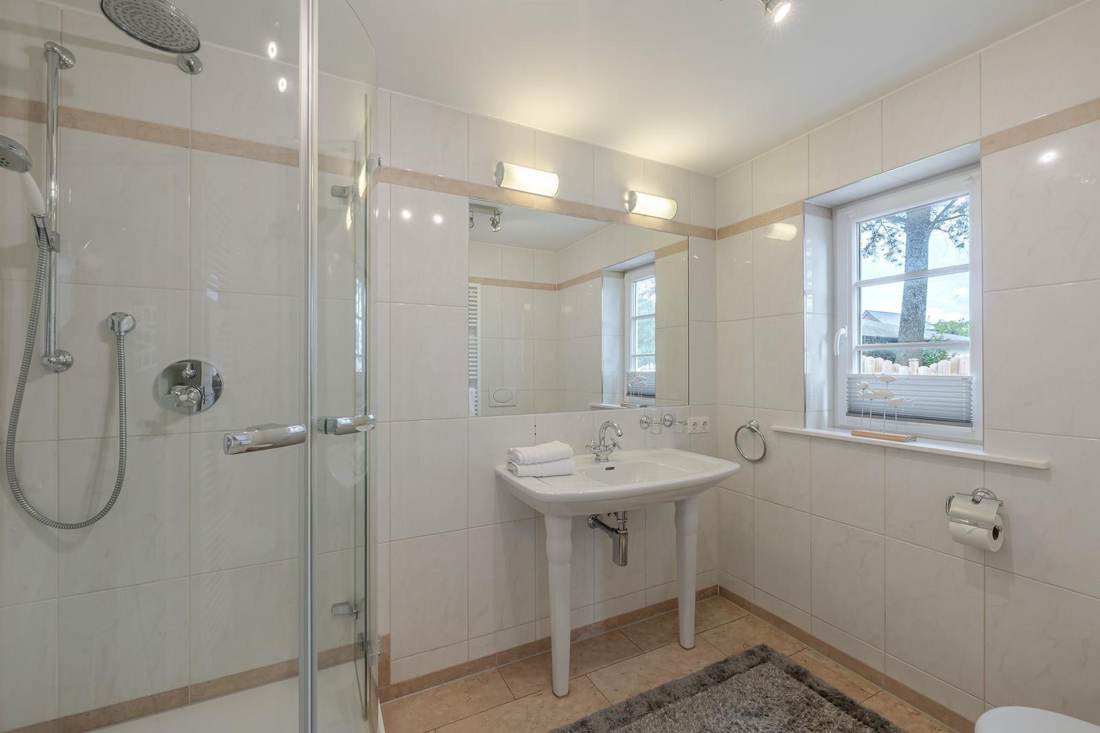 Bad mit Glasdusche, Standwaschbecken, großem Spiegel, Fenster und Handtüchern.