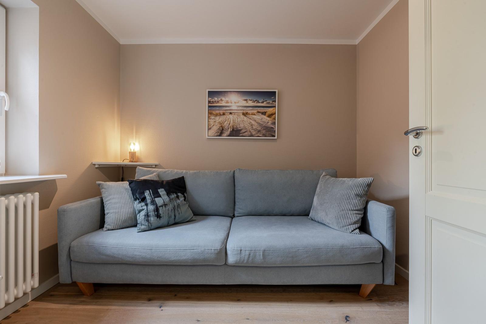Graues Sofa mit Kissen, Wandbild darüber, weiße Tür und Holzleuchte auf dem Regal.