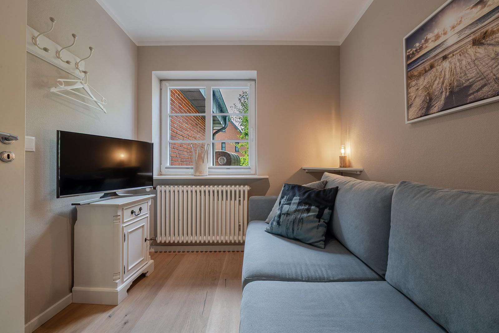 Helles Zimmer mit grauem Sofa, Fernseher auf weißem Sideboard und Fenster.