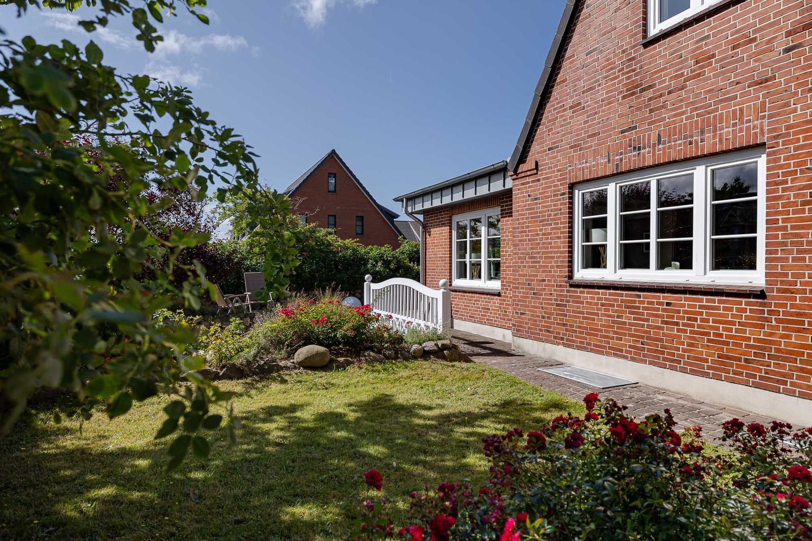 Garten mit Rasen, roten Rosen und Backsteinhaus mit Sprossenfenstern.