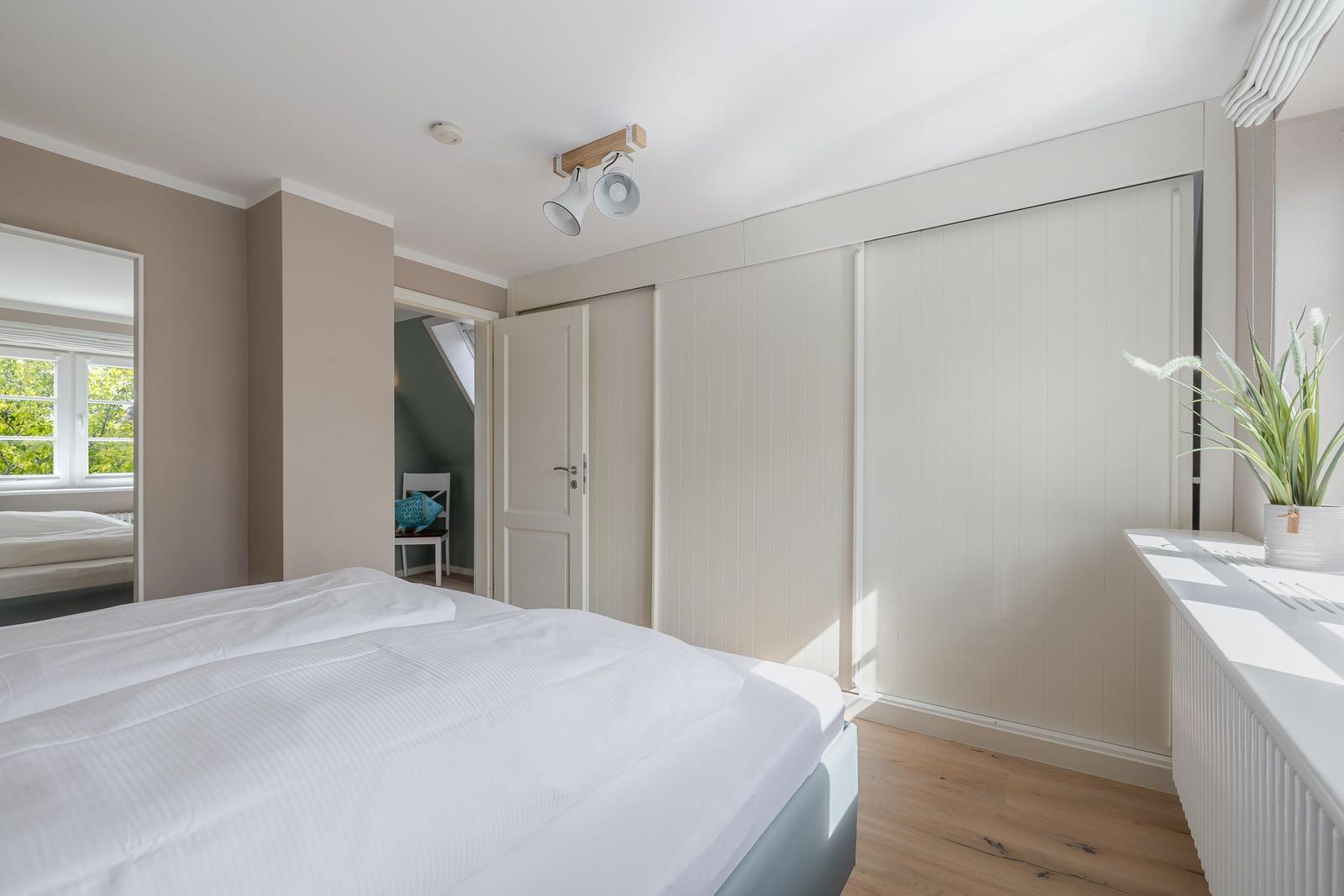 Schlafzimmer mit Doppelbett, weißem Schrank, Spiegel und Holzboden.