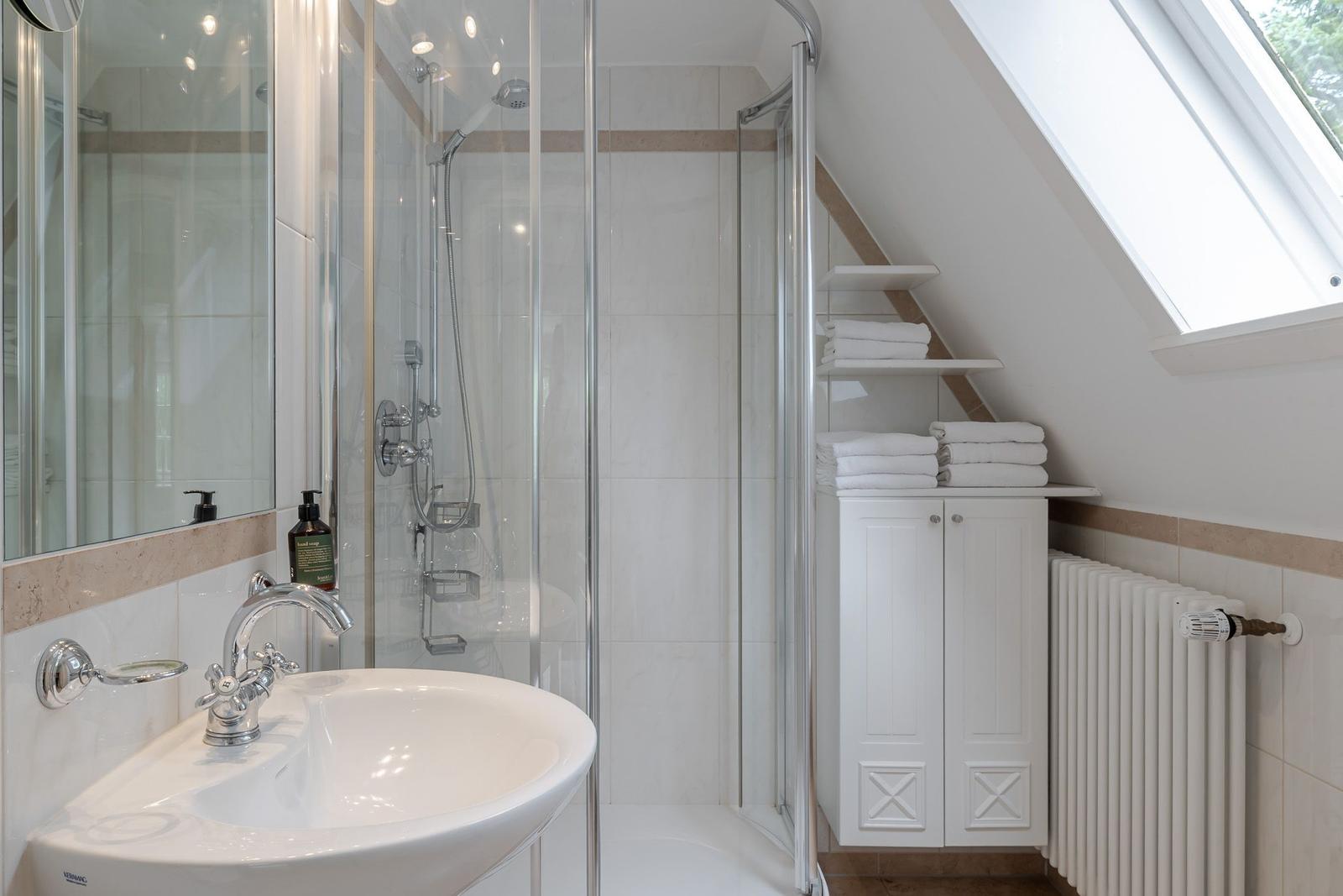 Badezimmer mit Waschbecken, Glasdusche, Handtüchern und Dachfenster.