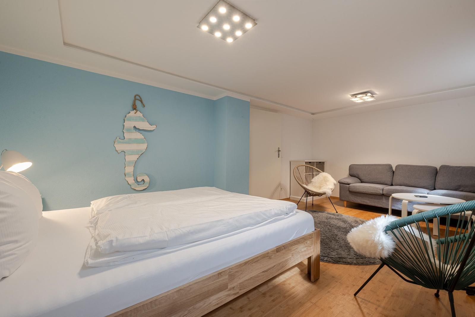 Wohnschlafbereich mit Holzbett, Seepferdchen an blauer Wand und Sofa.