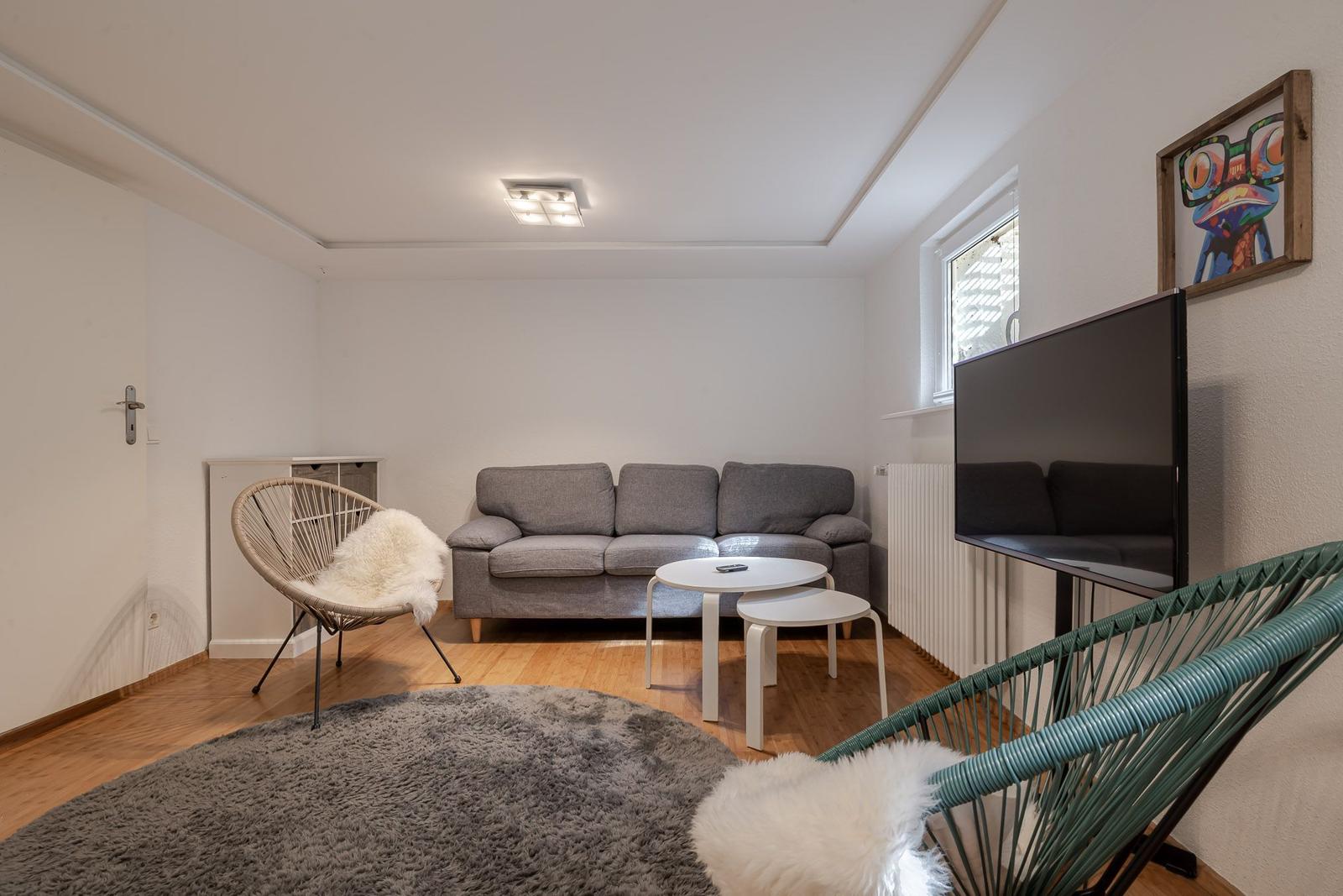 Wohnzimmer mit grauem Sofa, weißen Couchtischen, rundem Teppich und Fenster.