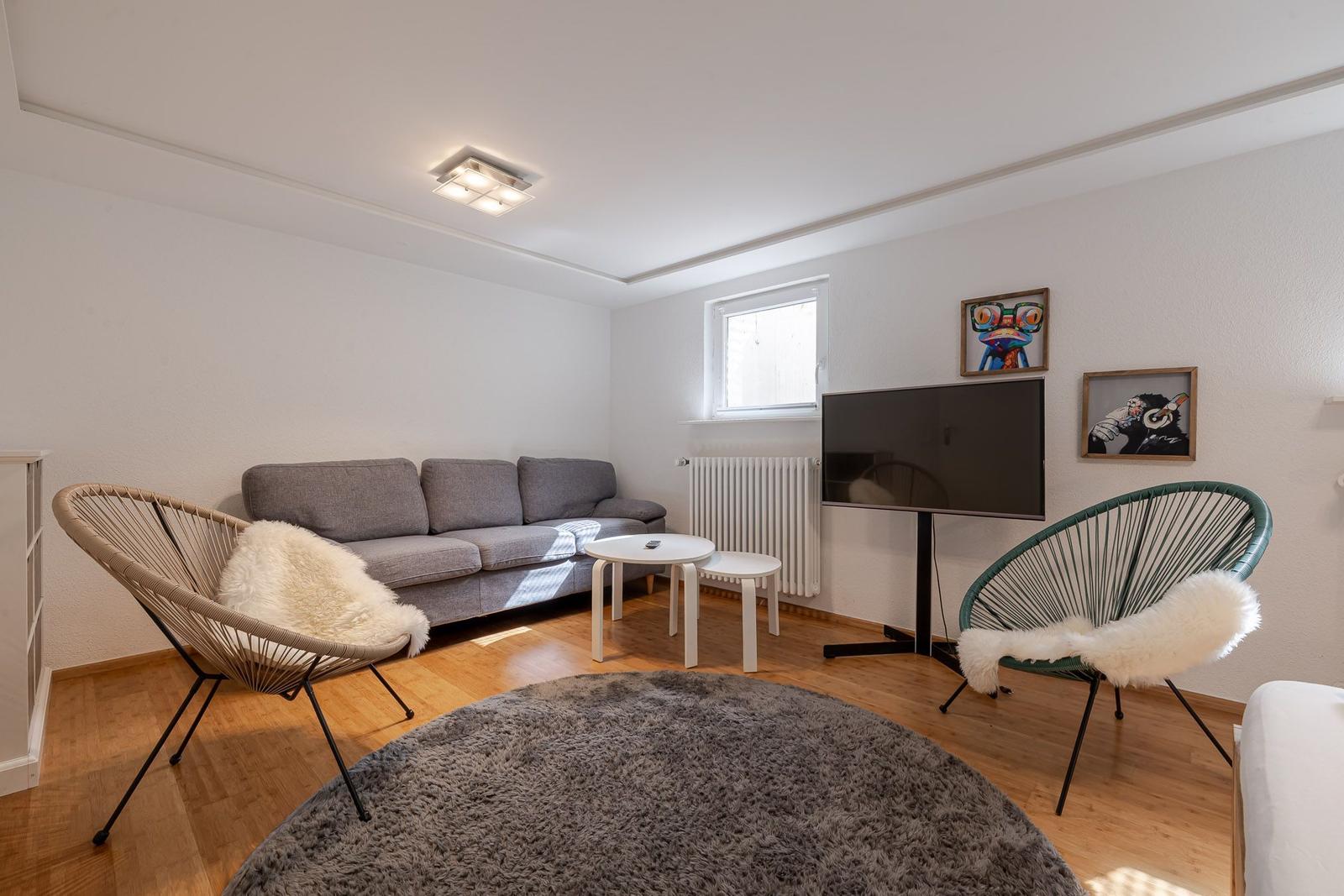 Wohnzimmer mit grauem Sofa, zwei Sesseln, rundem Teppich und Fernseher.