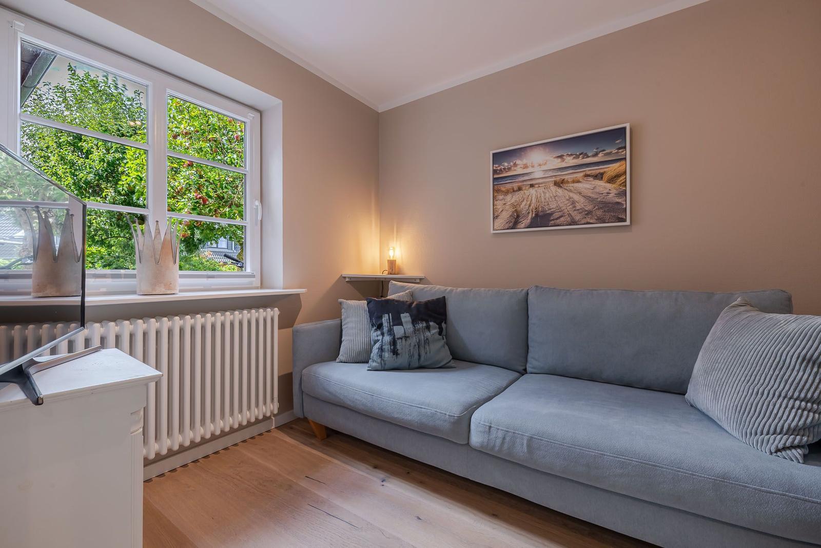 Hellblaues Sofa mit Kissen, Dünen-Wandbild und Fenster mit Heizkörper.