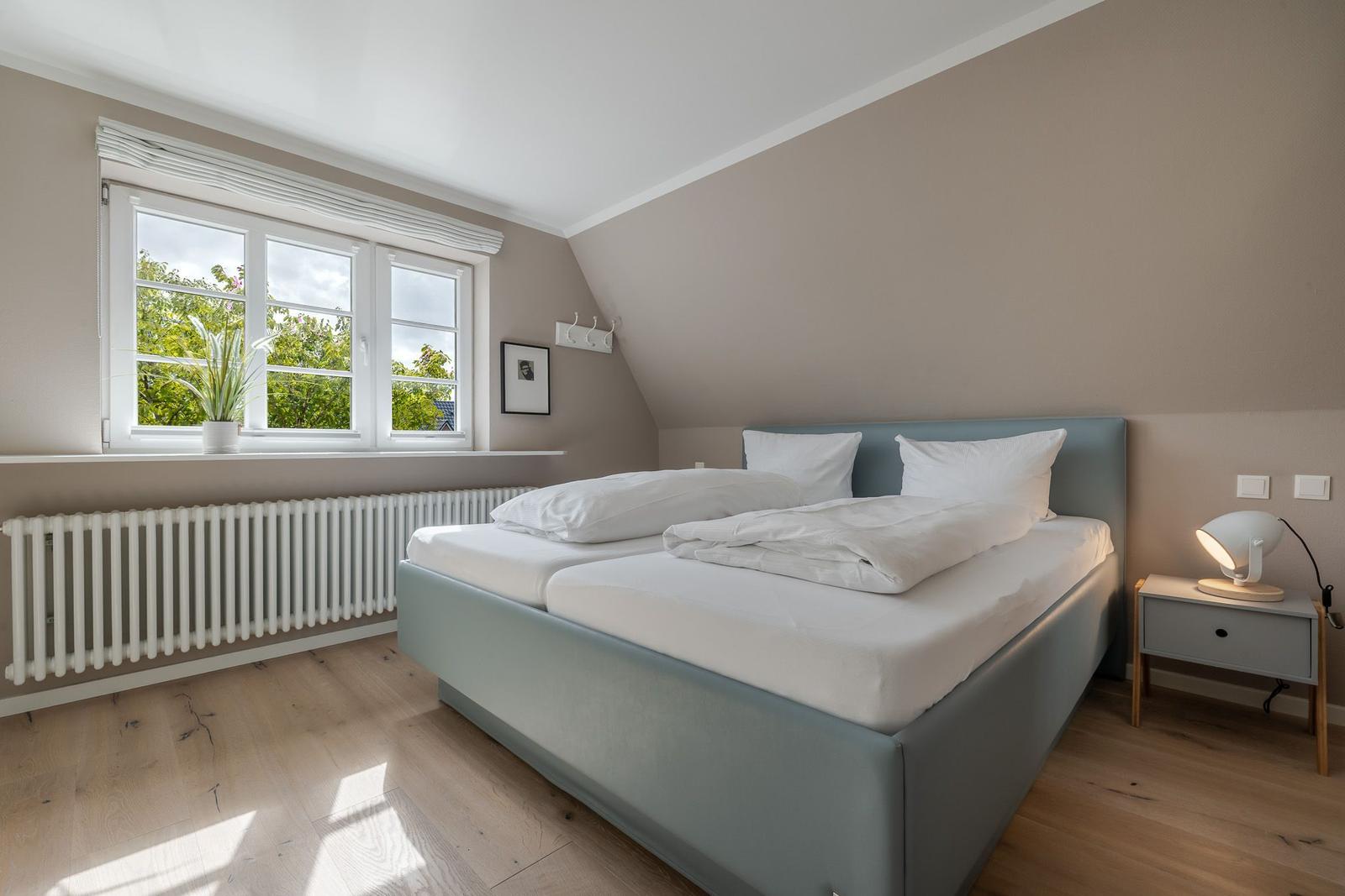 Schlafzimmer unter Schräge mit blaugrauem Bett, Fenster und Nachttisch.