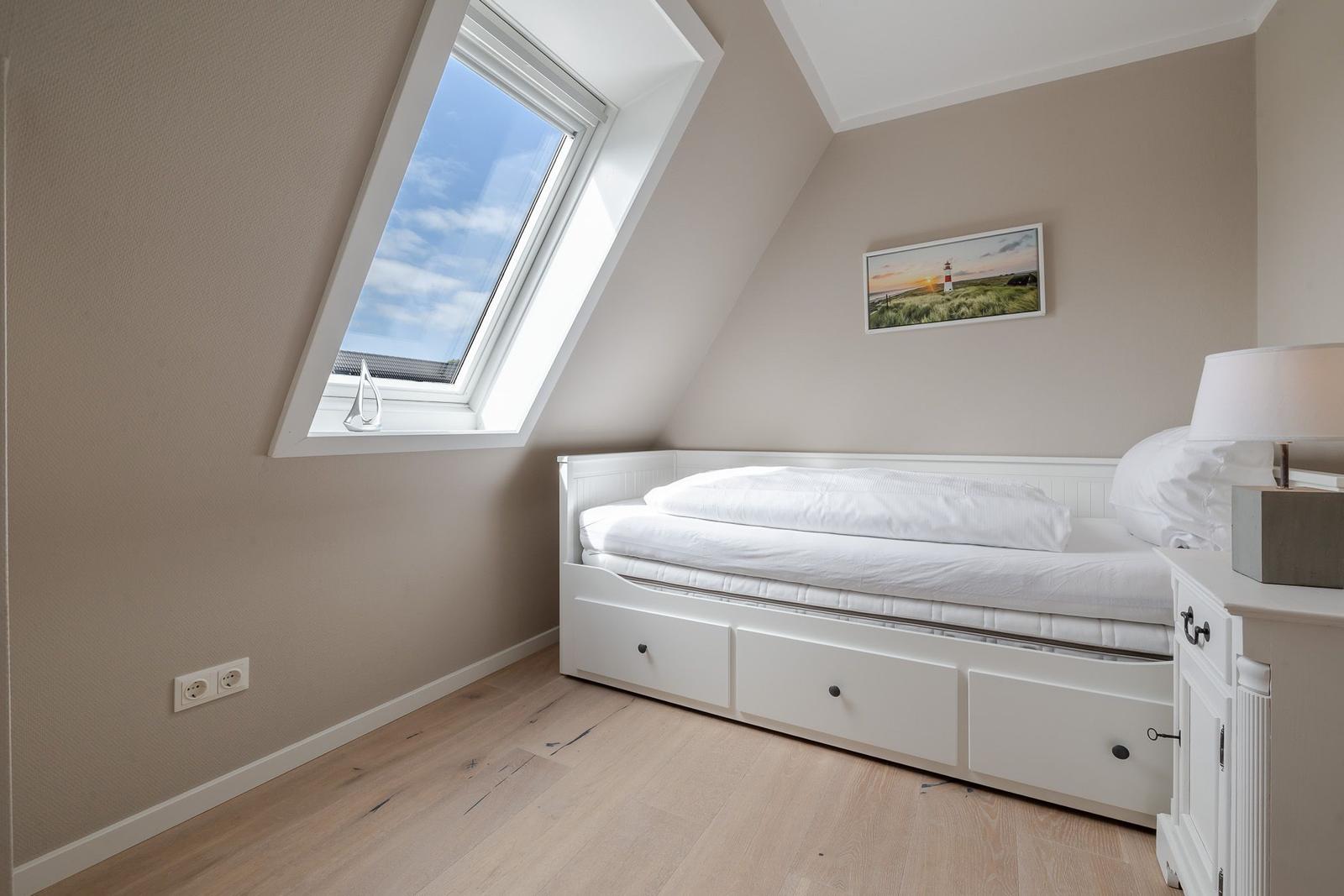 Dachzimmer mit weißem Bett, Schubladen, Dachfenster und Leuchtturm-Wandbild.