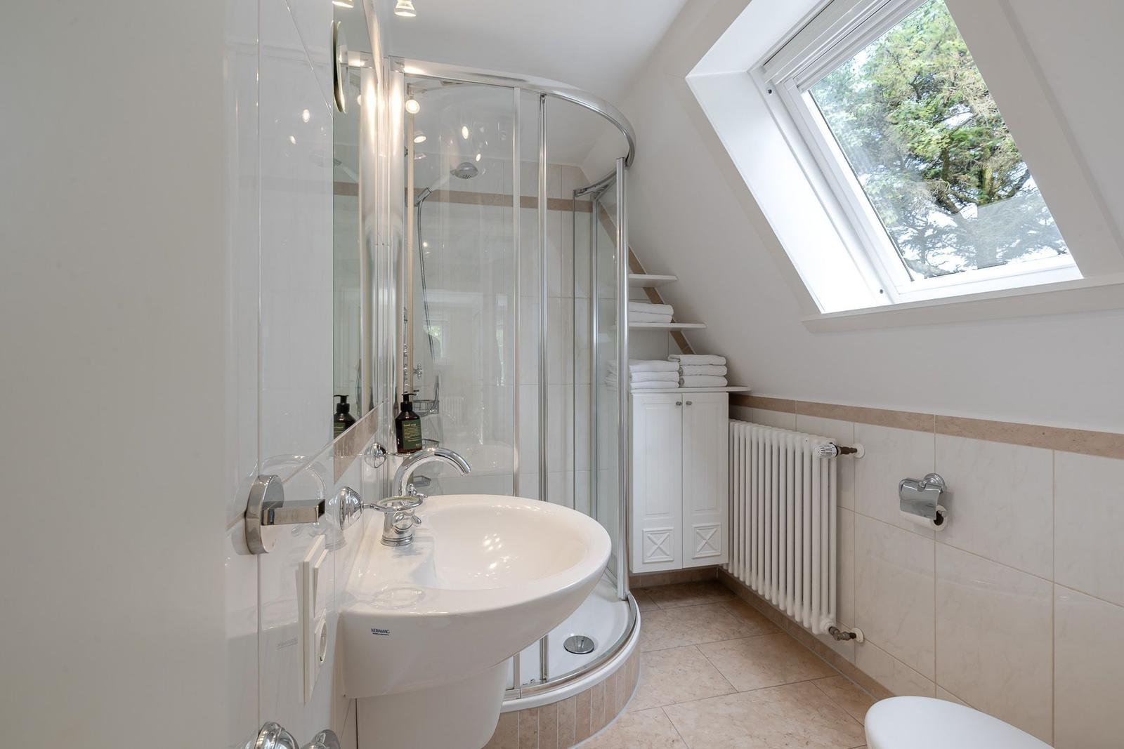 Dachbad mit Waschbecken, runder Glasdusche, Dachfenster und Handtüchern.
