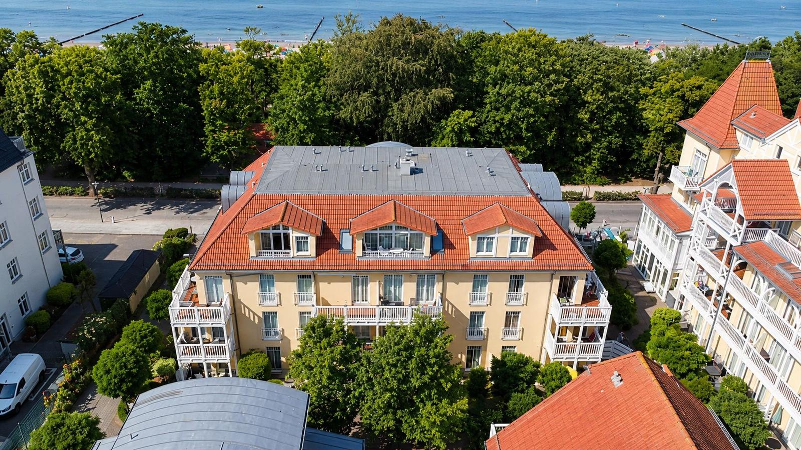 Haus mit rotem Dach und Balkonen, umgeben von Bäumen und Strand.