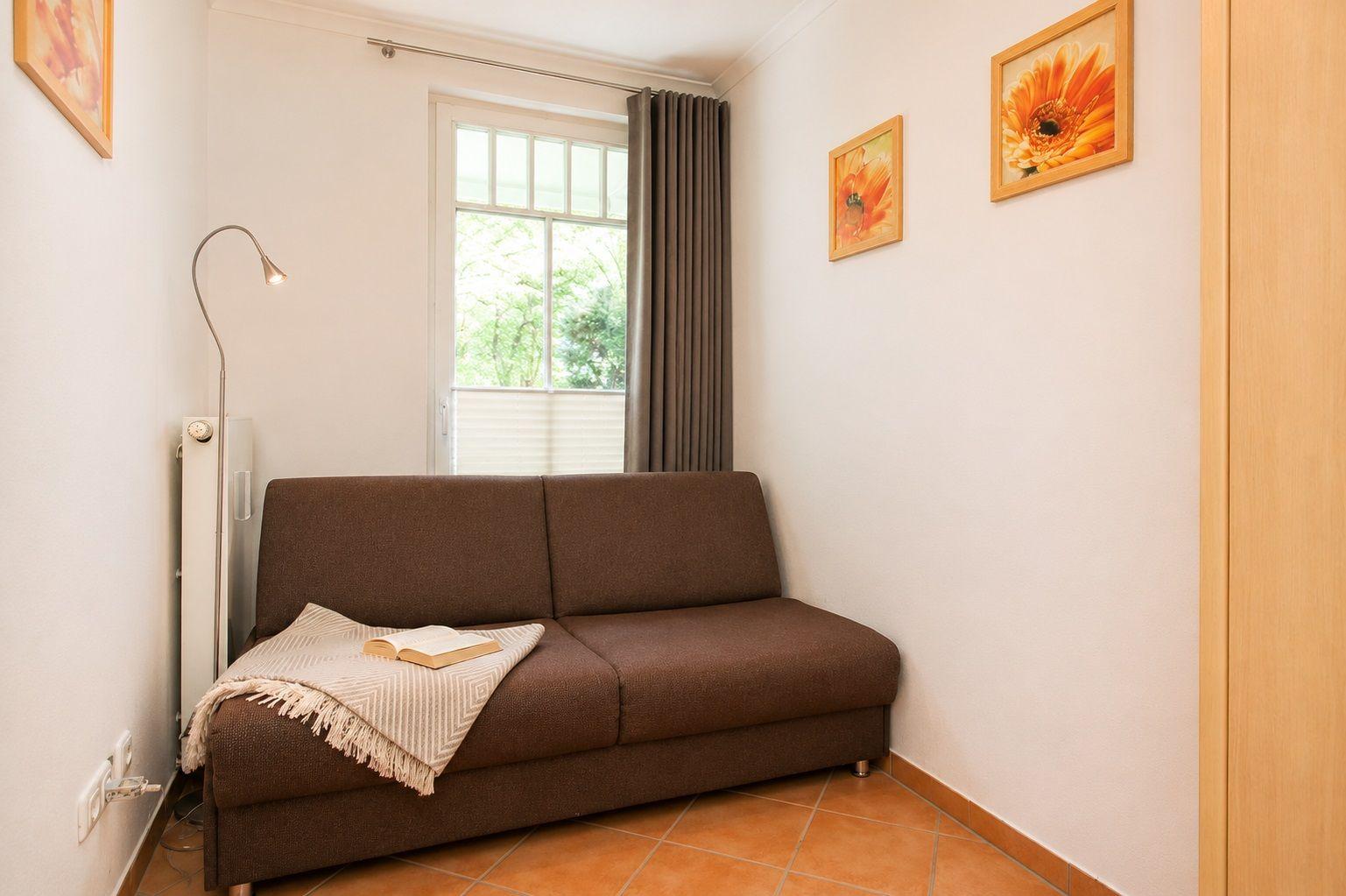 Ein Raum mit braunem Sofa, Fenster, Vorhang und Wandbildern.