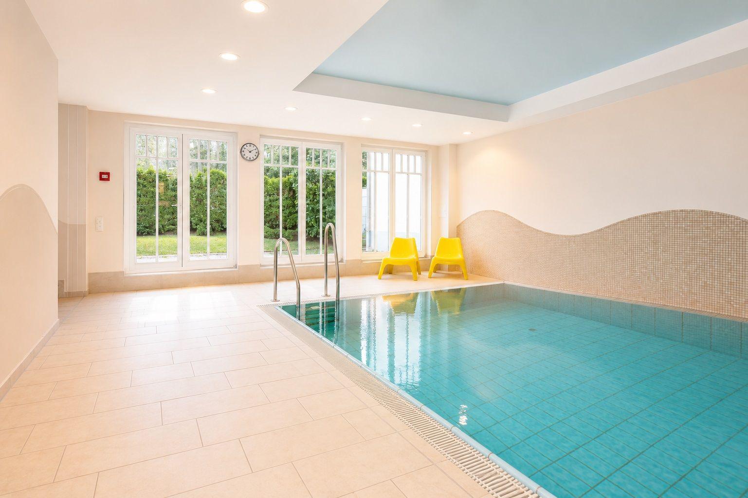 Innere Schwimmbad mit Pool, gelben Stühlen und Fenstern zum Garten.