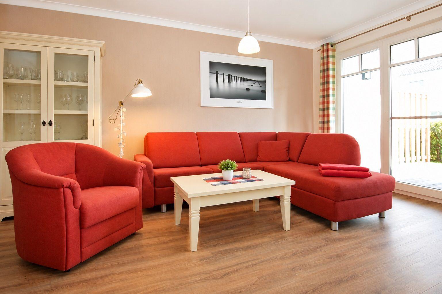 Ein Wohnzimmer mit rotem Sofa, weißem Couchtisch und Holzboden. An der Wand hängt ein Bild.