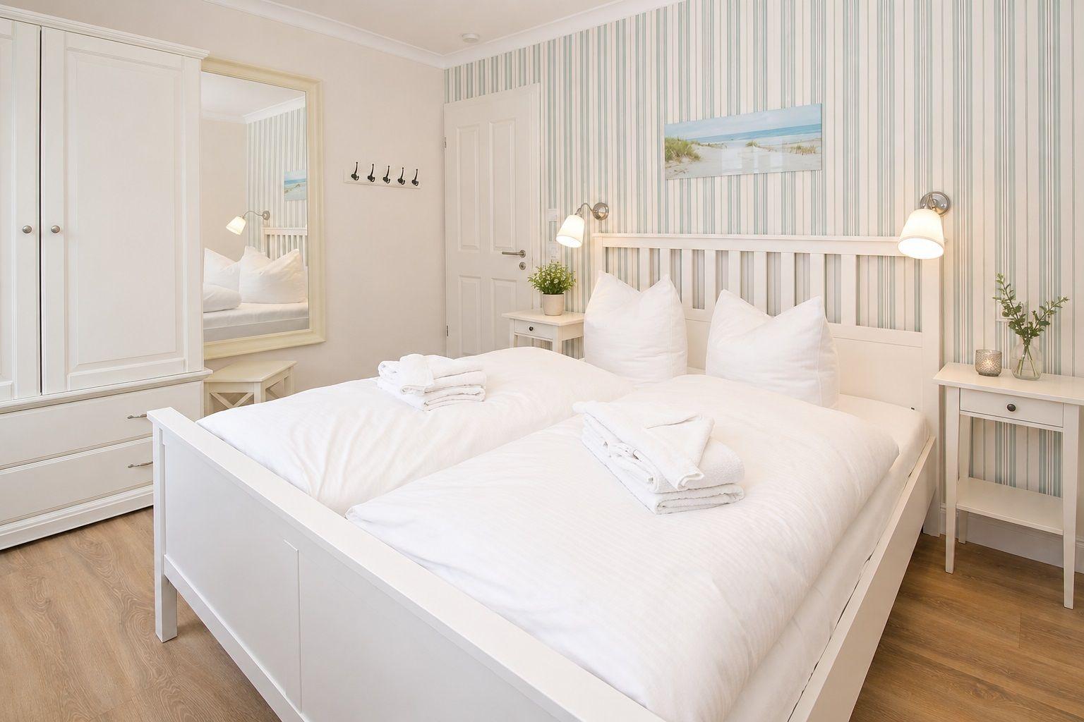 Schlafzimmer mit weißem Bett, Kleiderschrank und gestreifter Wandtapete.