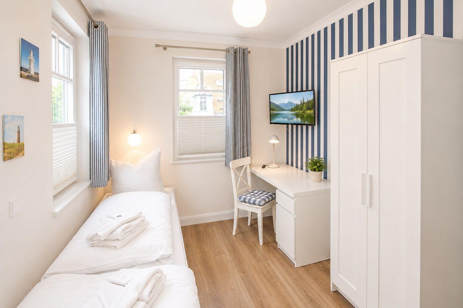 Schlafzimmer mit Bett, Schreibtisch, Kleiderschrank und Fenstern.