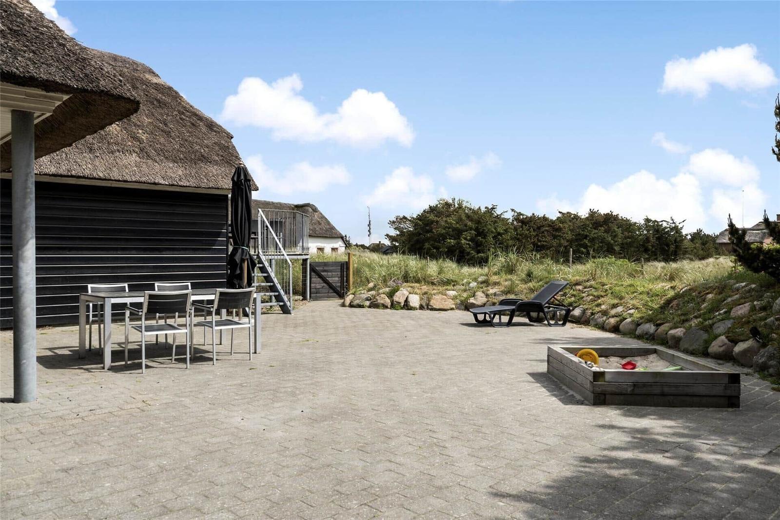 Terrasse mit Grill, Tisch und Stühlen vor schwarzem Holzhaus.