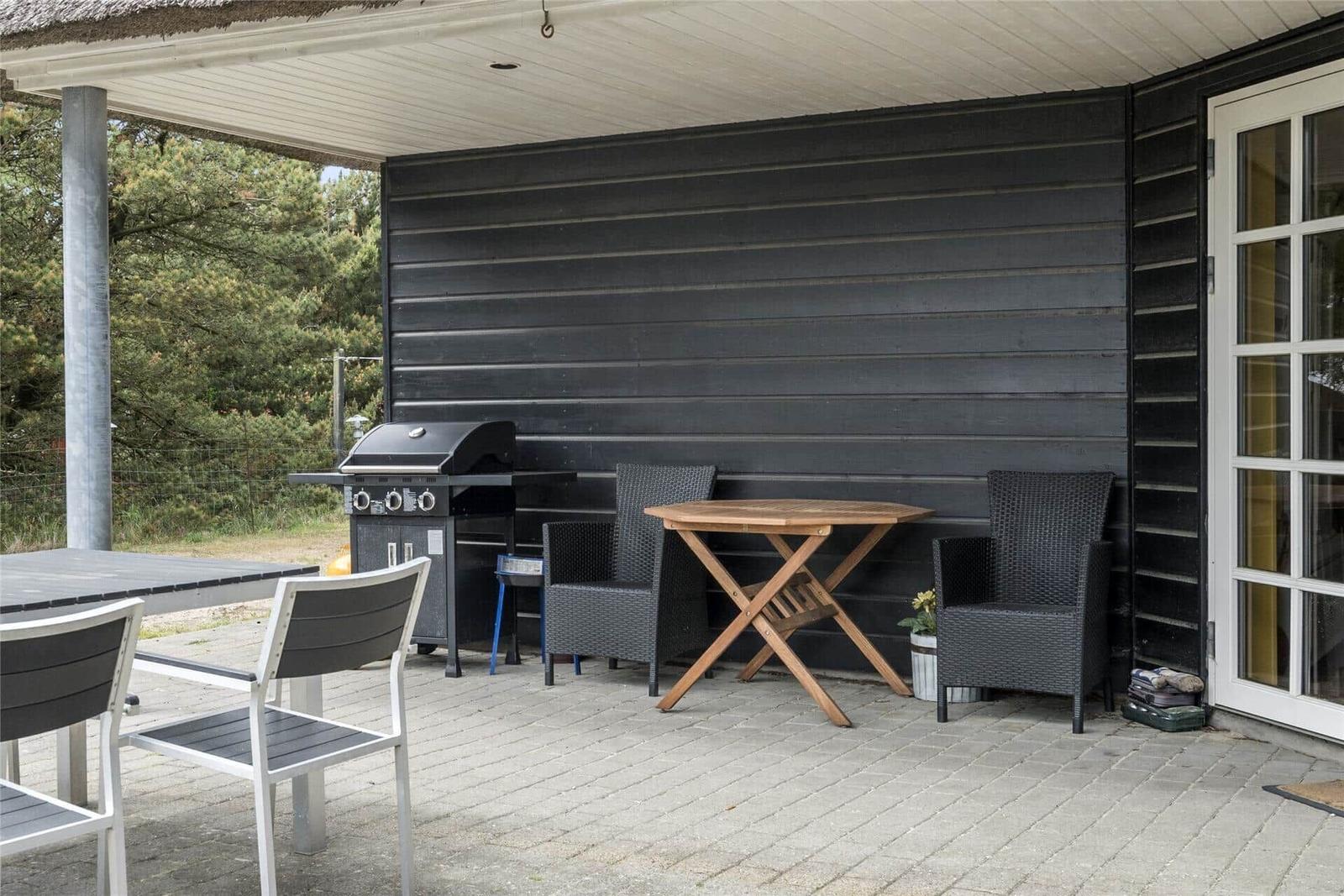 Schwarzes Strohdachhaus mit weißen Fenstern und Tür. Außenbereich mit Tisch und Stühlen.