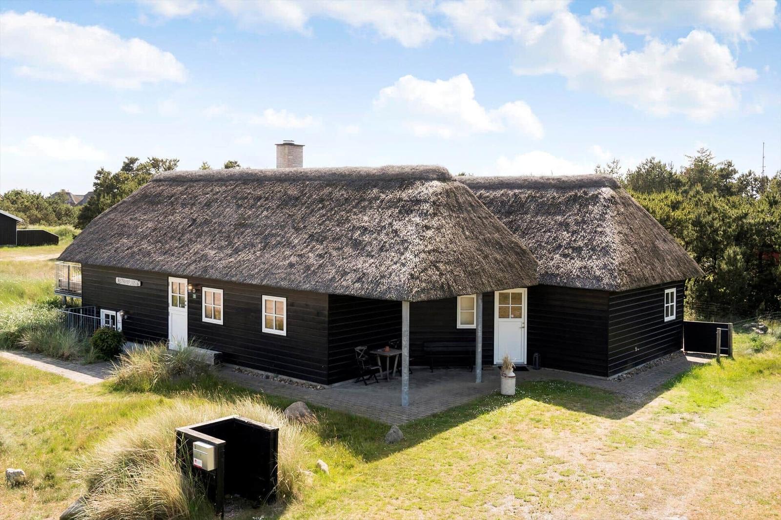 Haus mit strohgedeckten Dächern und weißer Tür. Außenbereich mit Tisch und Stühlen.